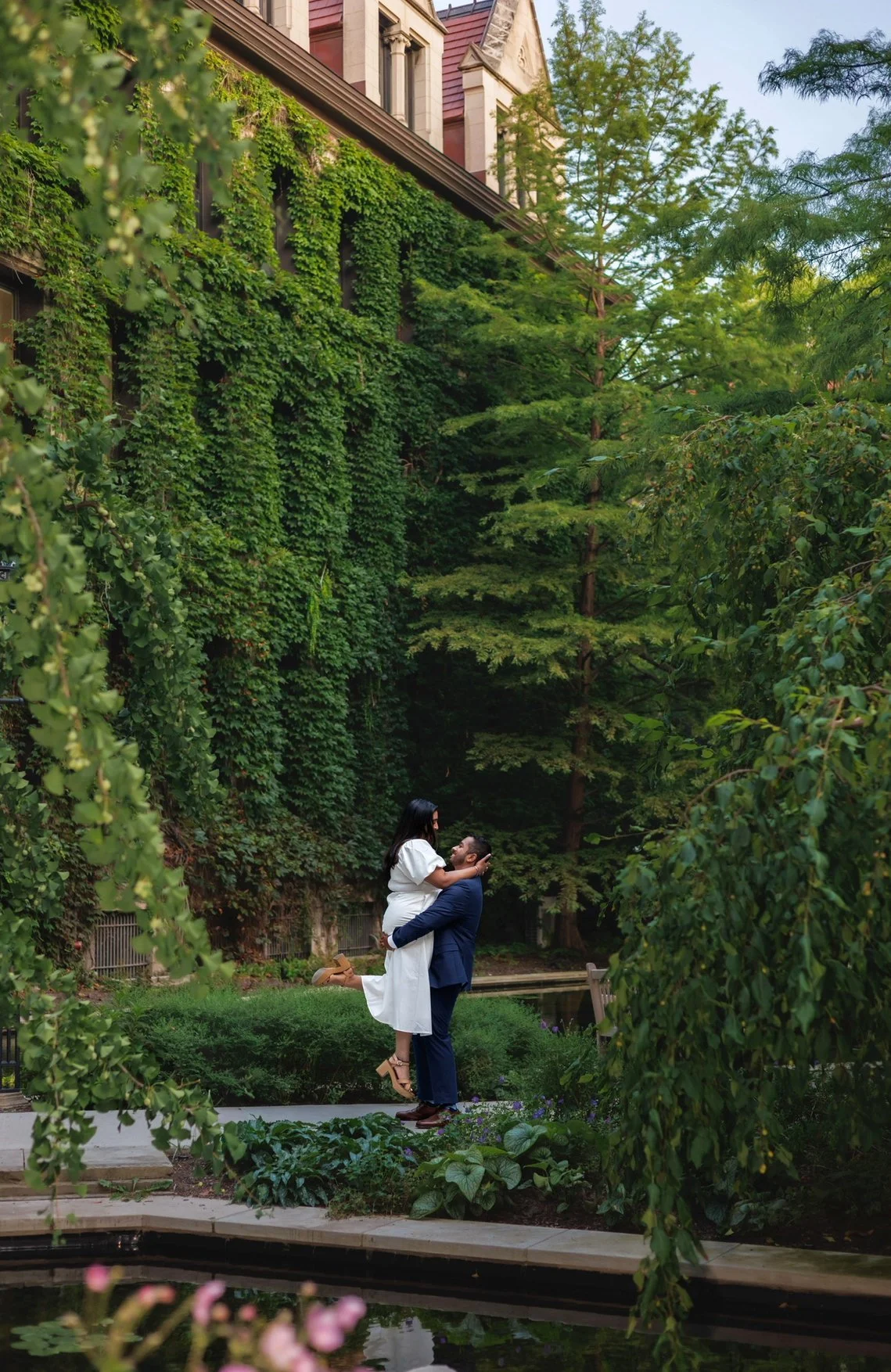 A couple walking hand in hand on a sidewalk, surrounded by columns, with the woman in a white dress and the man in a patterned shirt.