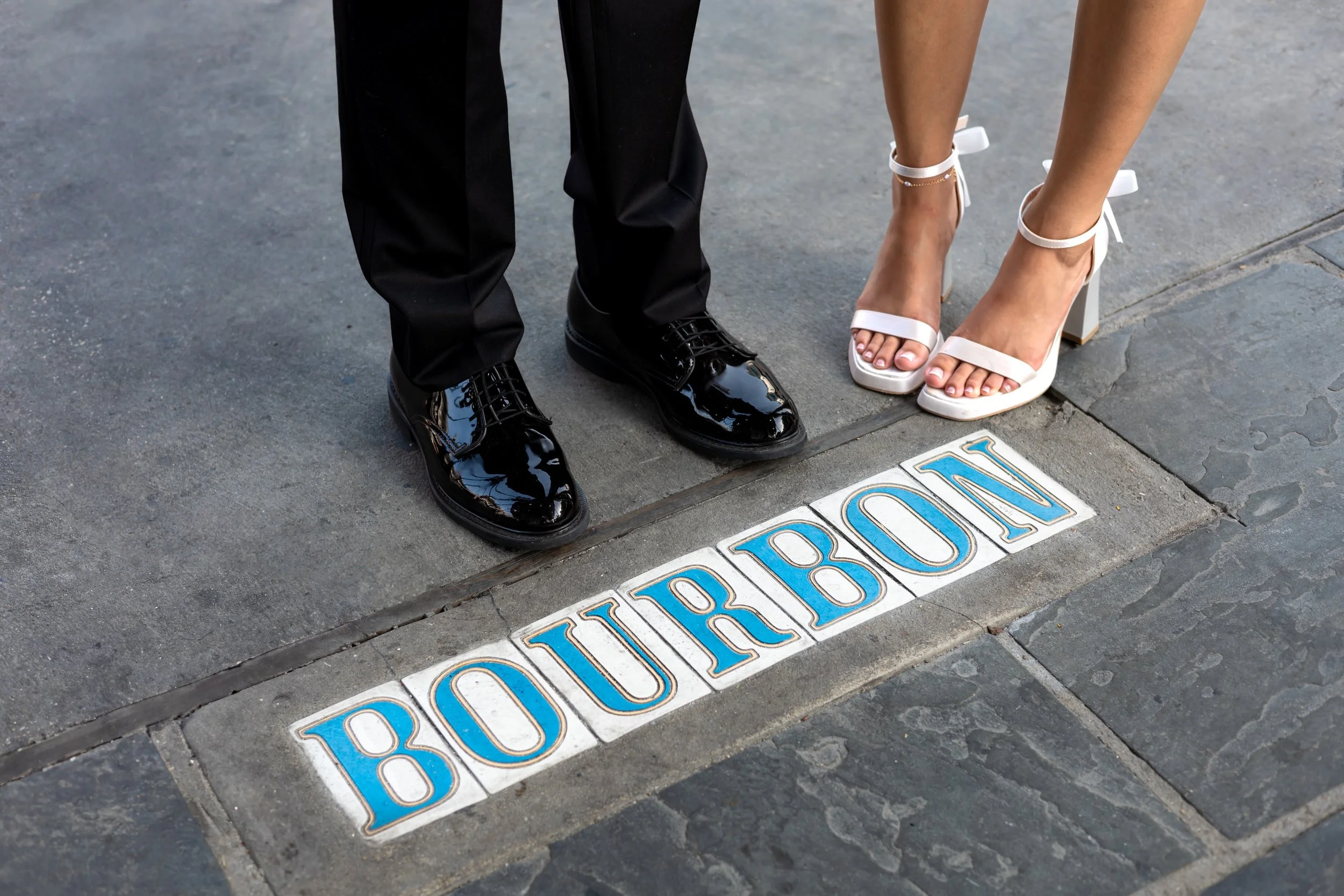 Close-up of a couple's legs and shoes on a city sidewalk, with the word 'BOURBON' spelled out on a decorative tile embedded in the pavement. Chicago wedding photographer