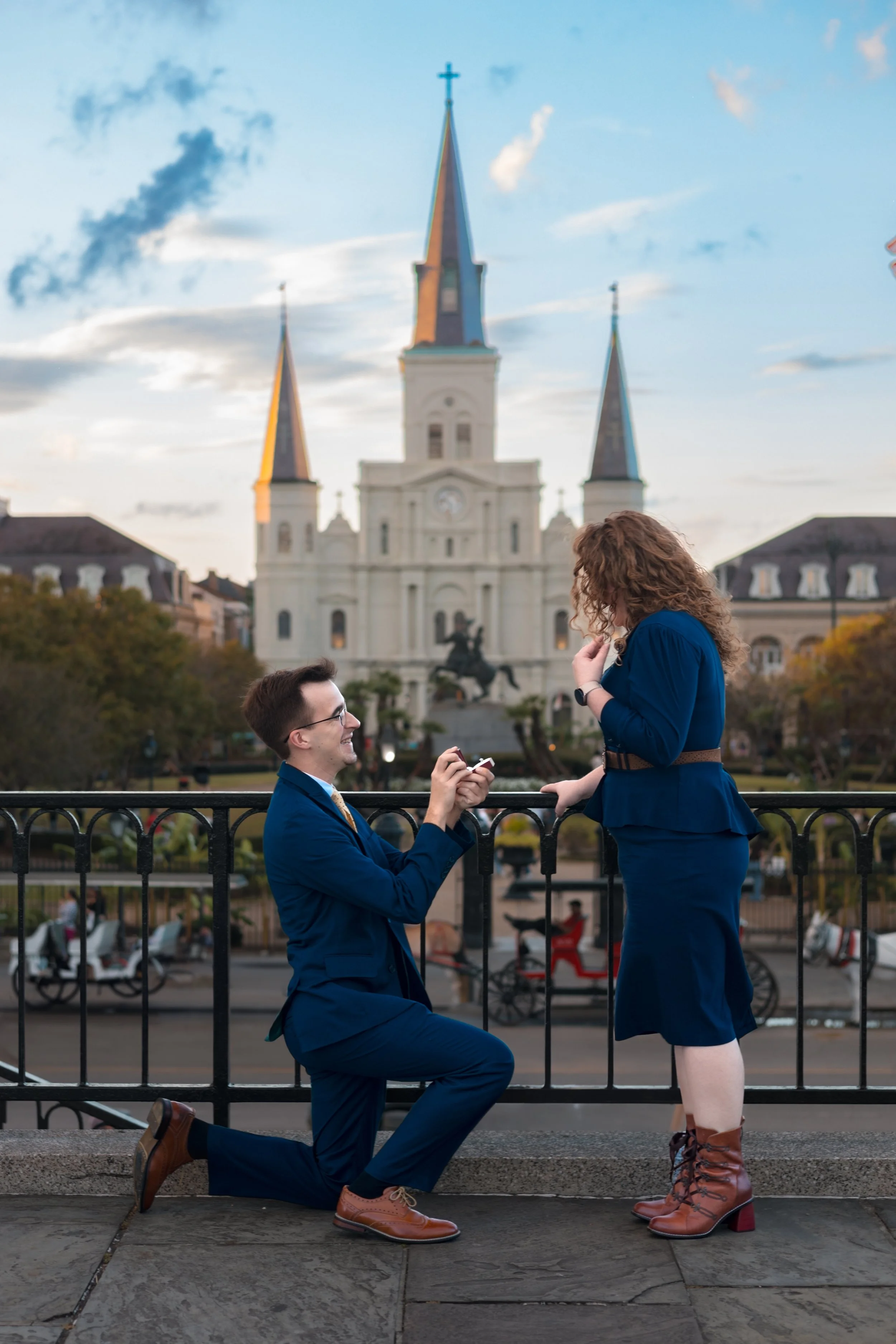 Man proposing on one knee in front of St. Louis Cathedral in New Orleans while partner reacts during a surprise proposal