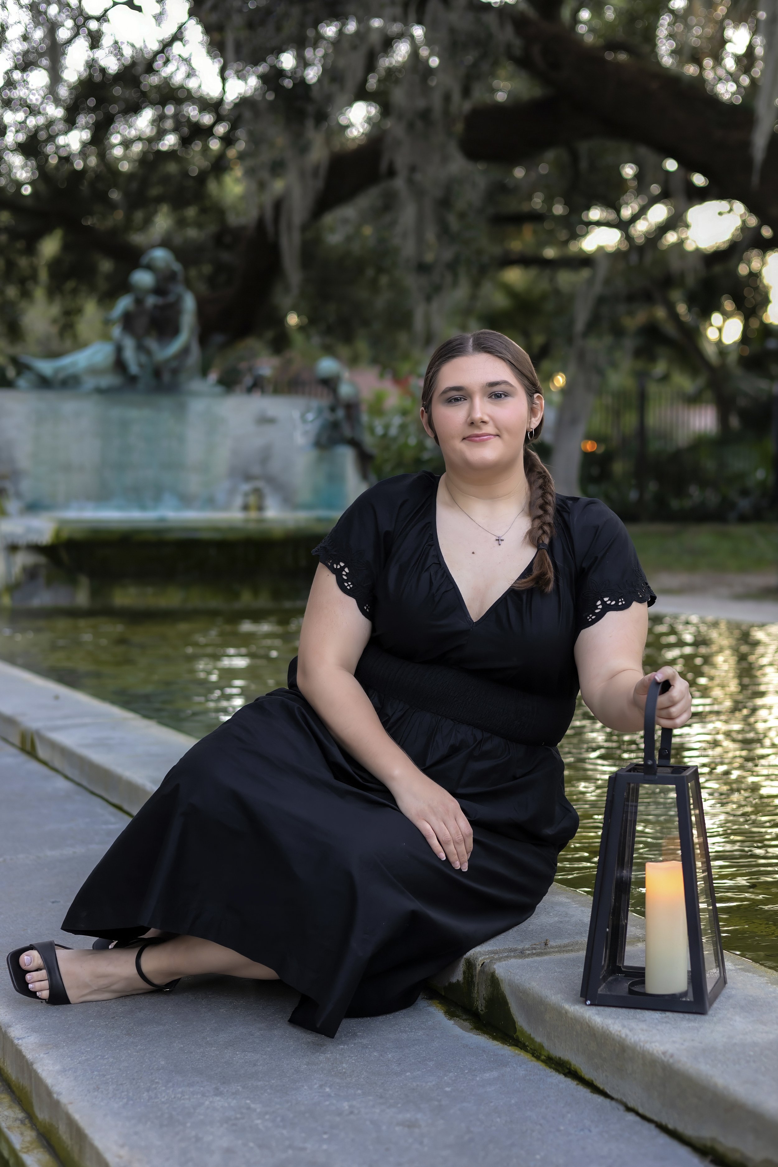 Woman in black dress holding lantern by a fountain