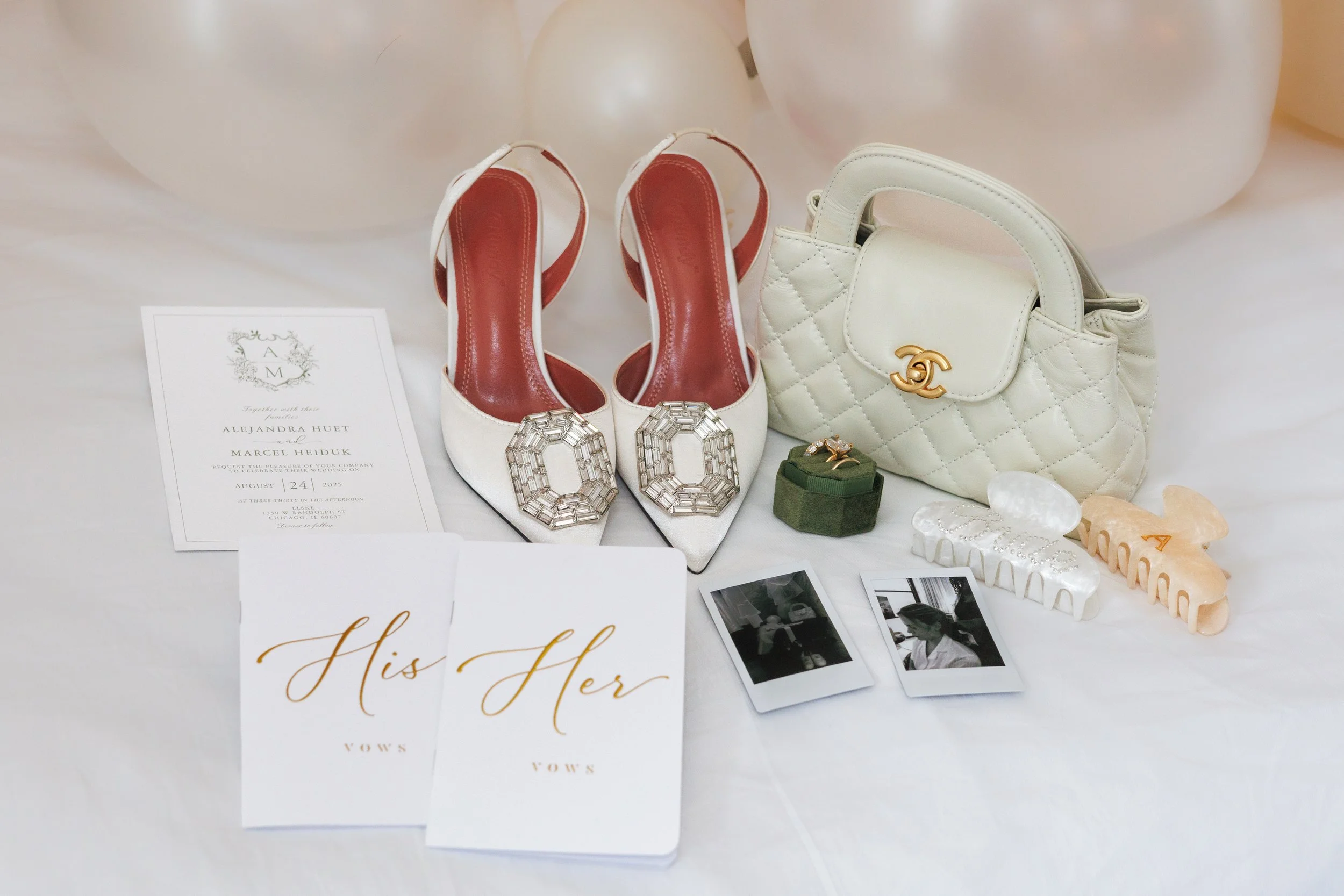 Flat lay of wedding details including rings, shoes, and vow books arranged on a bed with soft white balloons