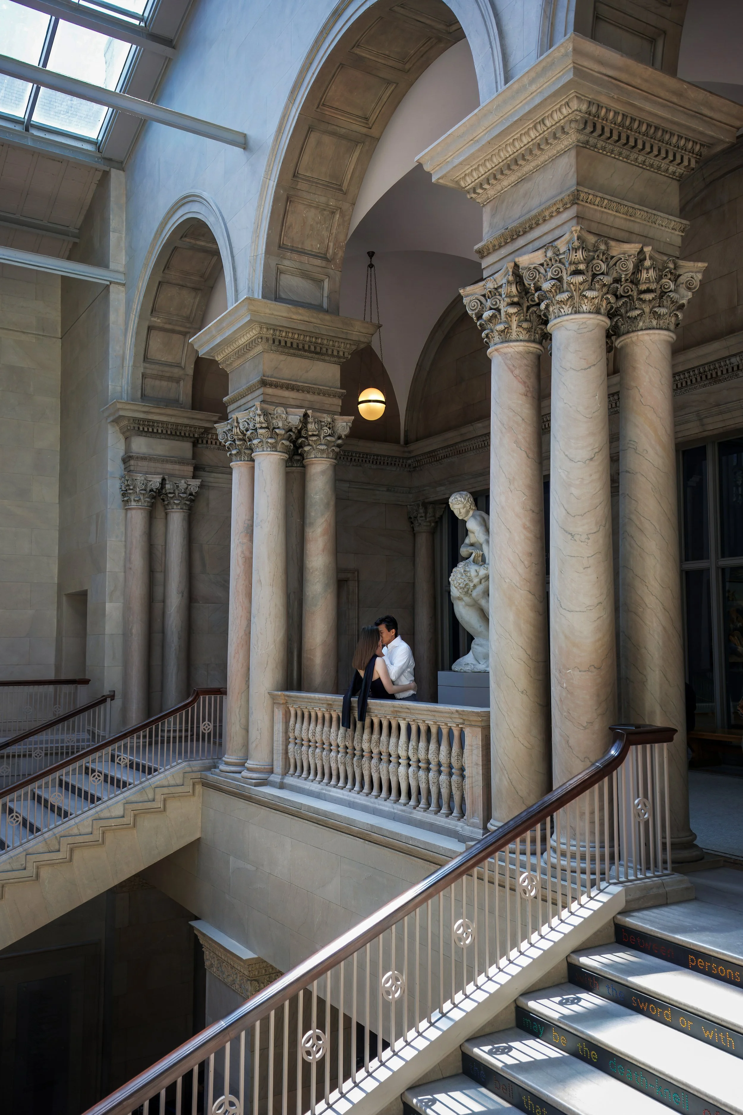 Couple embracing on a marble balcony inside the Art Institute of Chicago, surrounded by grand columns, sweeping staircases, and classical architecture bathed in natural light.