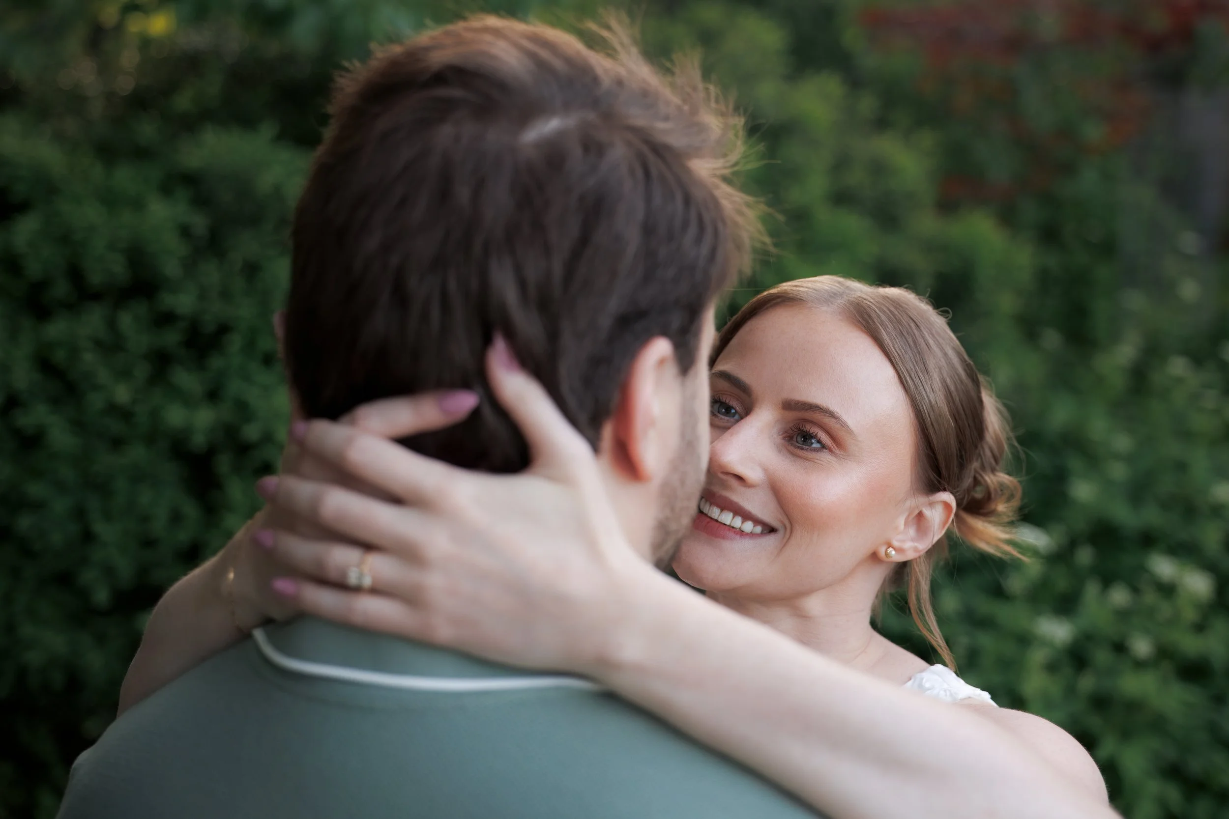 I couple looking into each other eyes with her hards resting on the back of his neck to show off their engagement ring. 