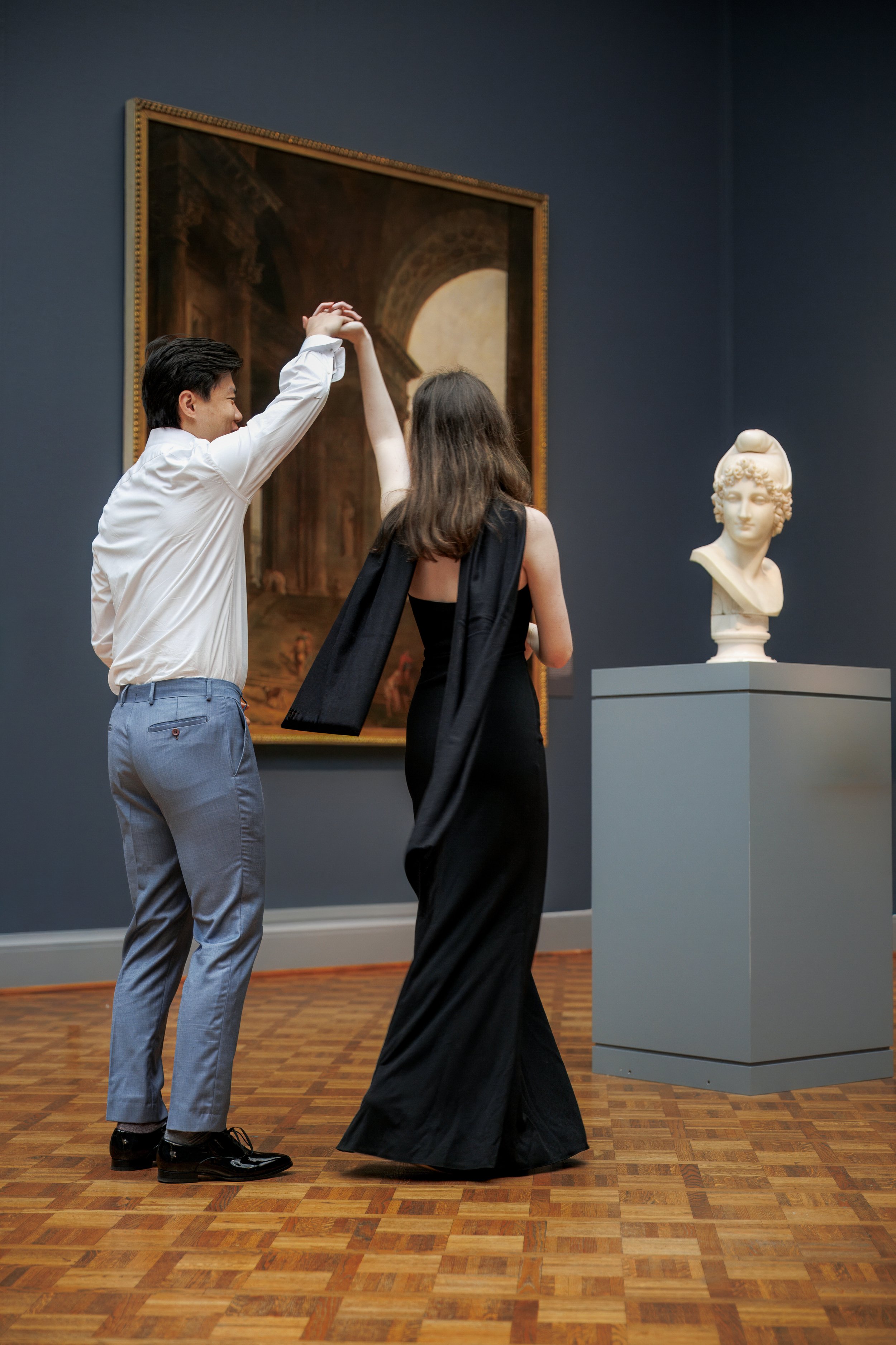 Couple dancing through the Art Institute of Chicago gallery, passing paintings and sculpture beneath moody blue walls and museum light.