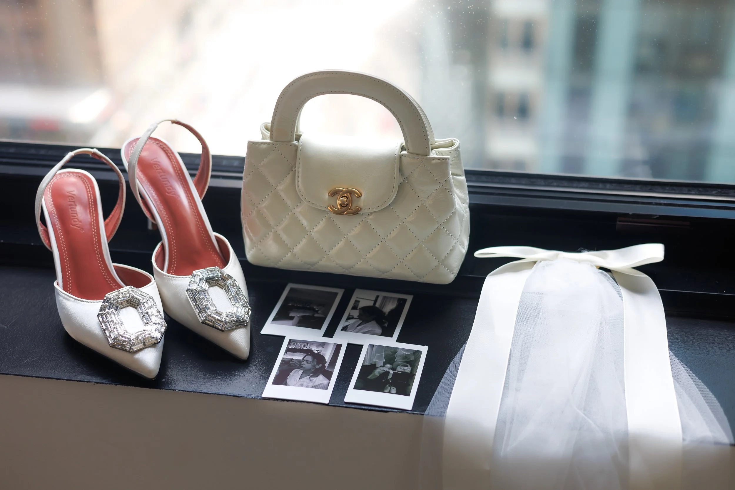 Chicago wedding photographer captures a lay flat in front of a window with rings, shoes, a bag, veil, and polaroids 