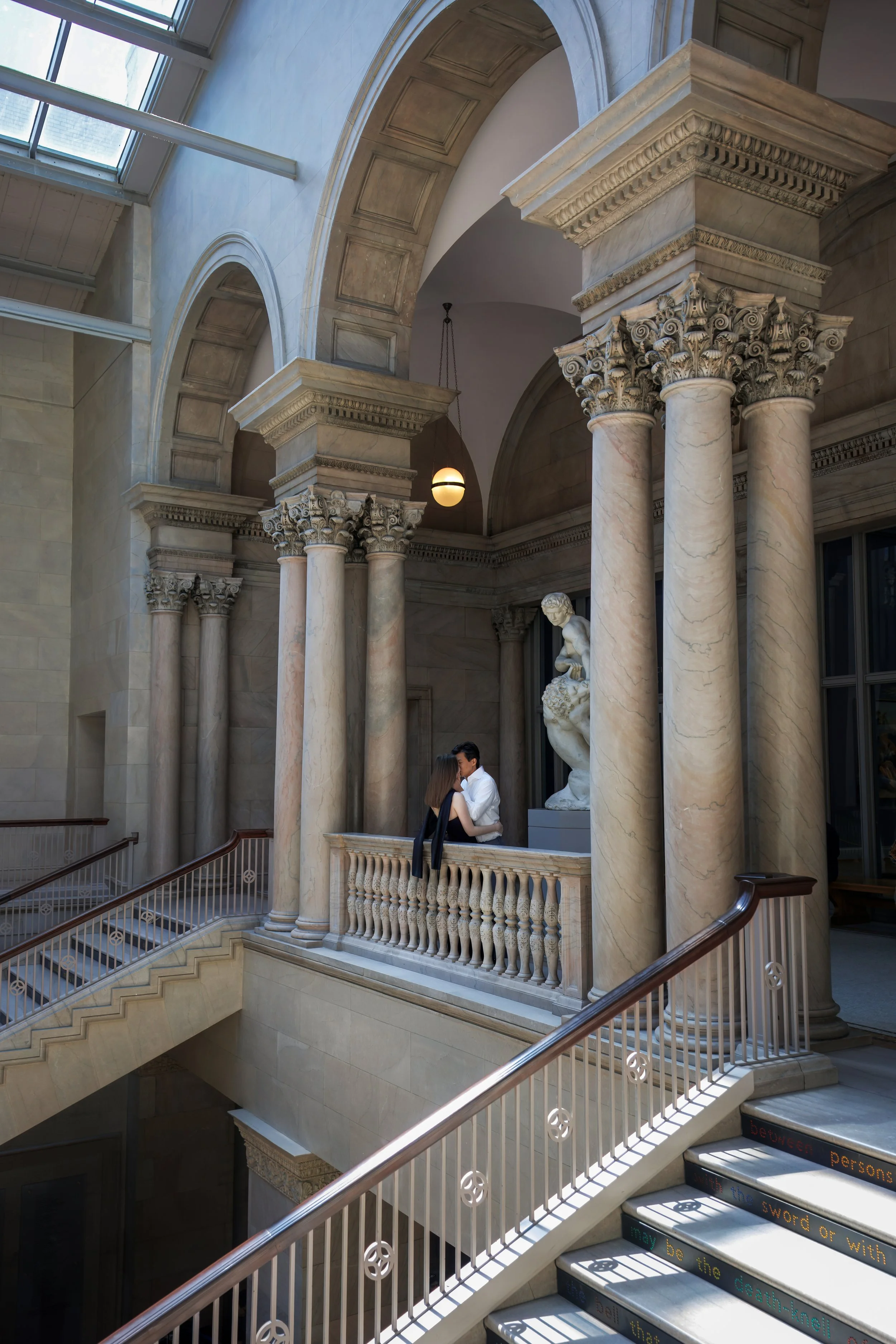 Elegant engagement couple kissing beneath grand marble columns and arches inside the Art Institute of Chicago during a romantic Chicago engagement photo session.