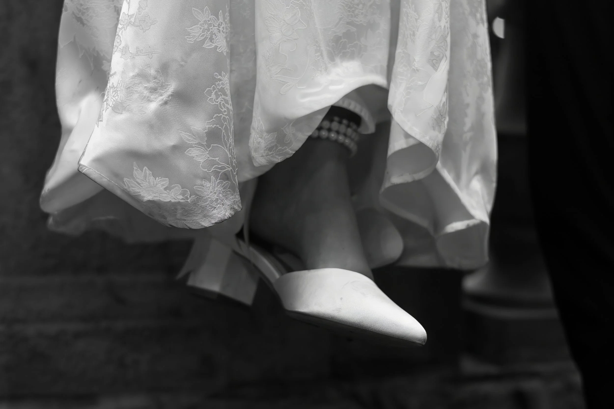 A bride's legs and feet in pointed white shoes, with a pearl bracelet on the ankle, as she stands beneath her wedding dress with lace detailing. Chicago wedding photographer