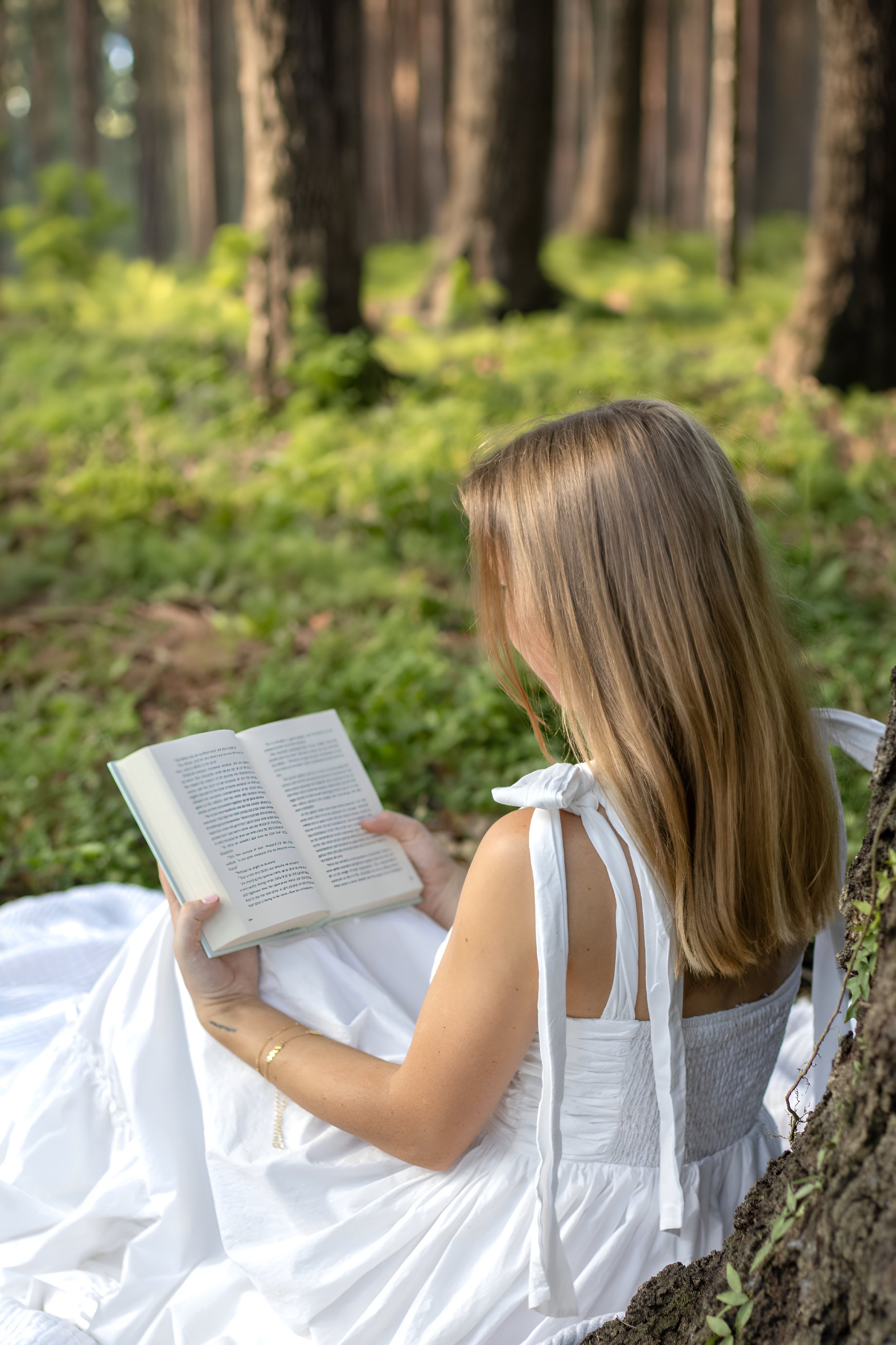Woman in a white dress reading a book in a forest