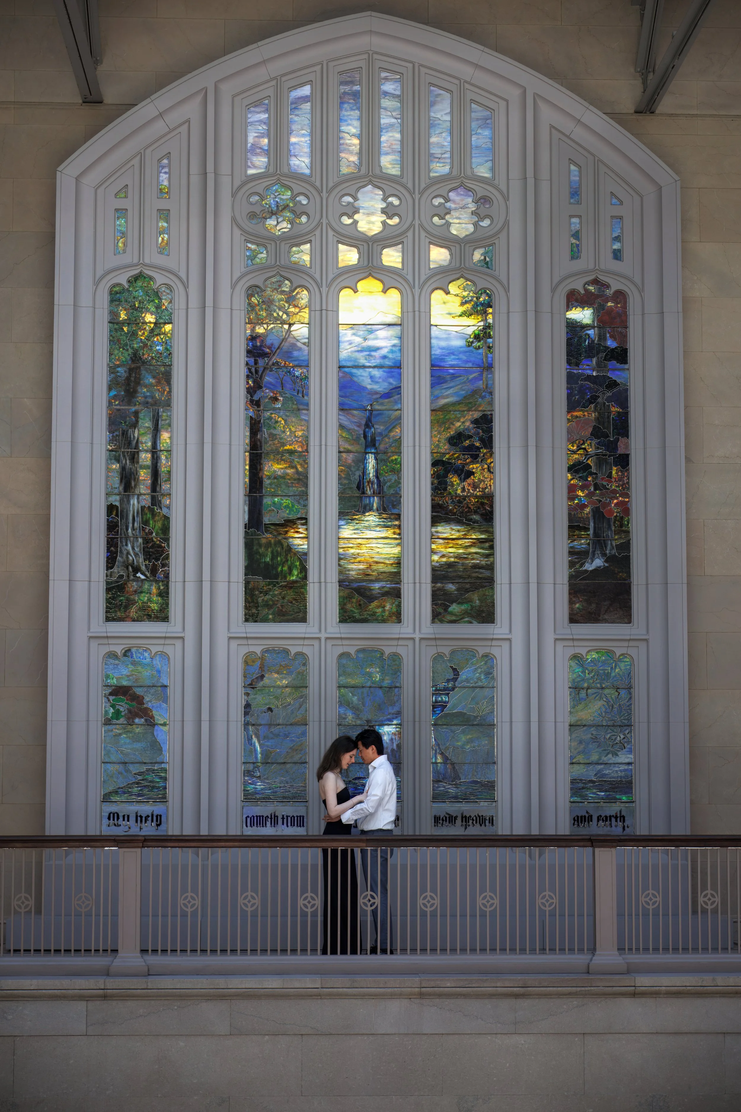 Couple embracing beneath a towering stained glass window inside the Art Institute of Chicago, surrounded by light, symmetry, and timeless architecture.