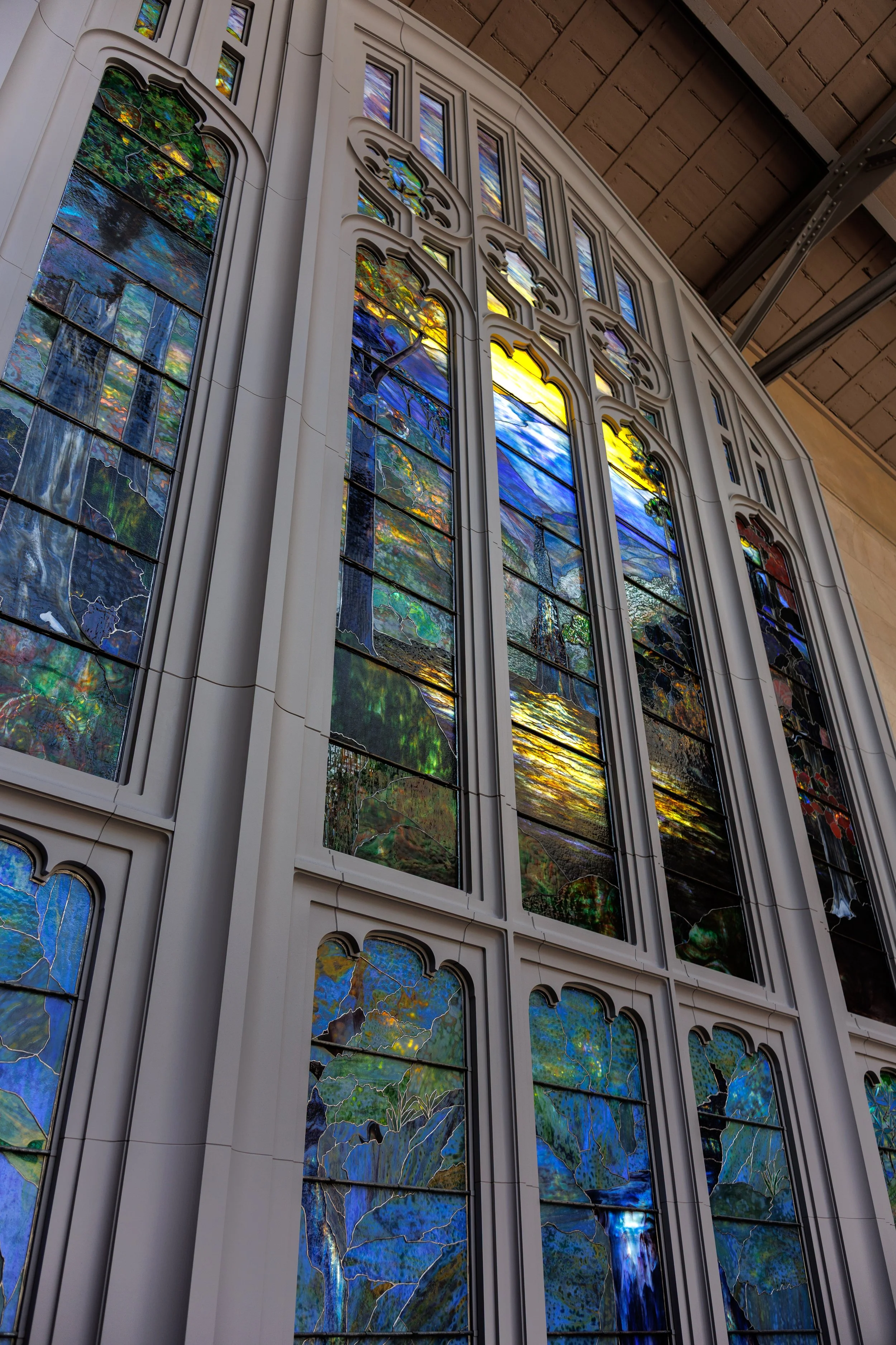 Colorful stained glass windows in a church or cathedral, with intricate designs and natural scenery depicted.