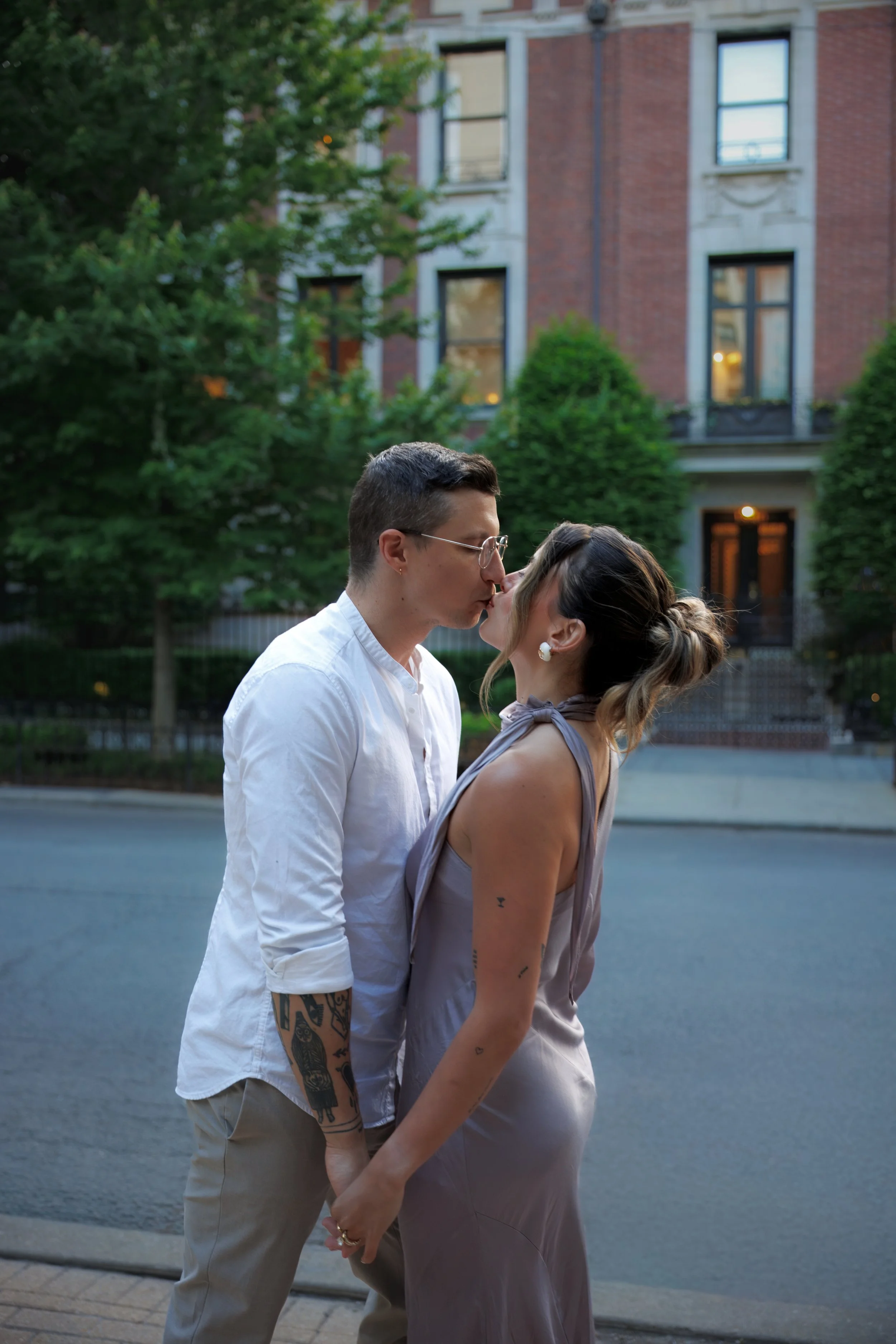 Couple holding hands and leaning in for a kiss on a tree-lined Chicago street surrounded by historic architecture.