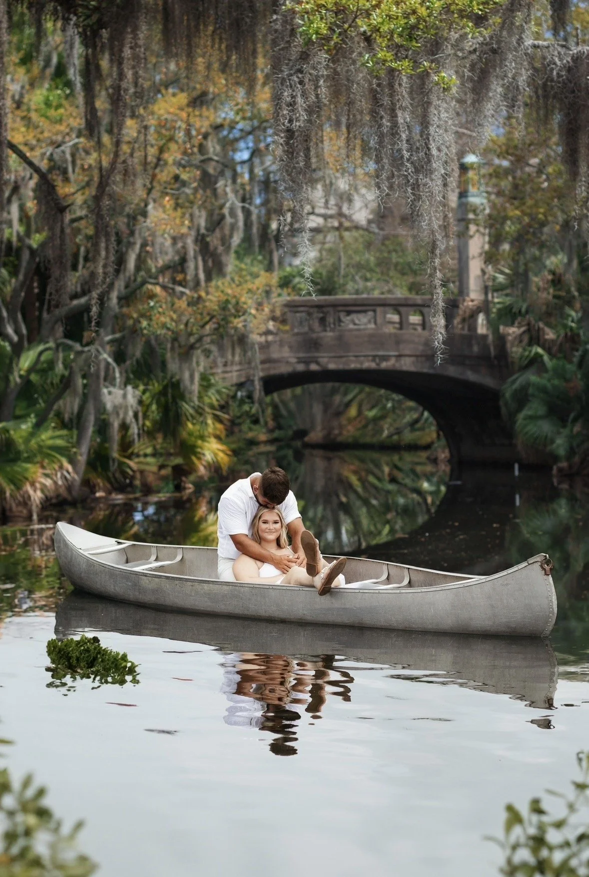 Chicago wedding photographer captures a couple in a canoe on a calm river surrounded by trees with Spanish moss, with a bridge in the background.