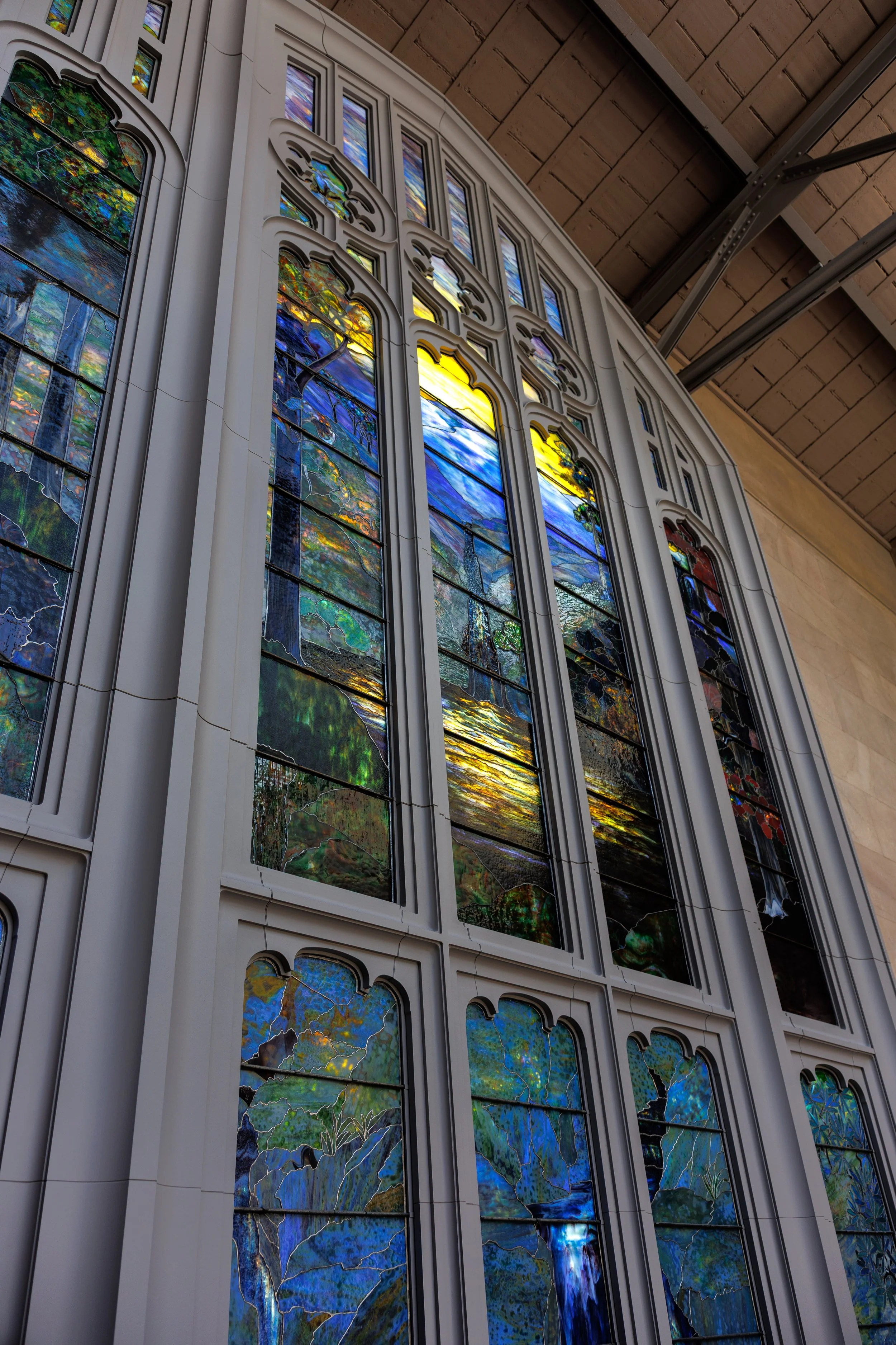 Colorful stained glass windows in a church or cathedral, with intricate designs and various vibrant colors, viewed from below.