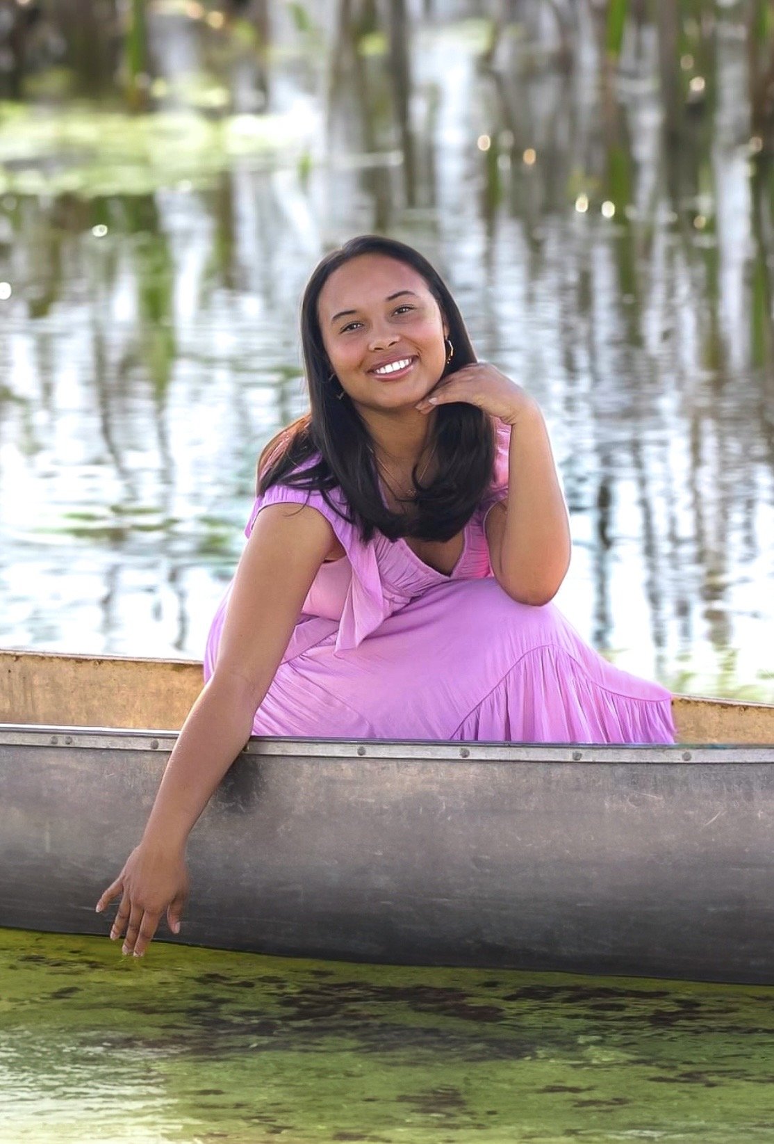 Woman in purple dress sitting in a canoe on a body of water, touching the water surface.
