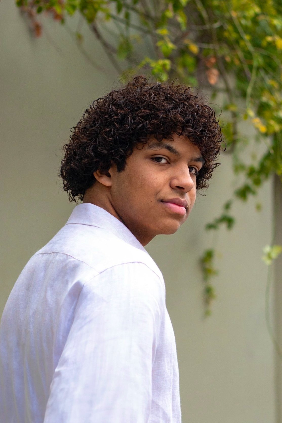 Person with curly hair in white shirt looking over shoulder outdoors