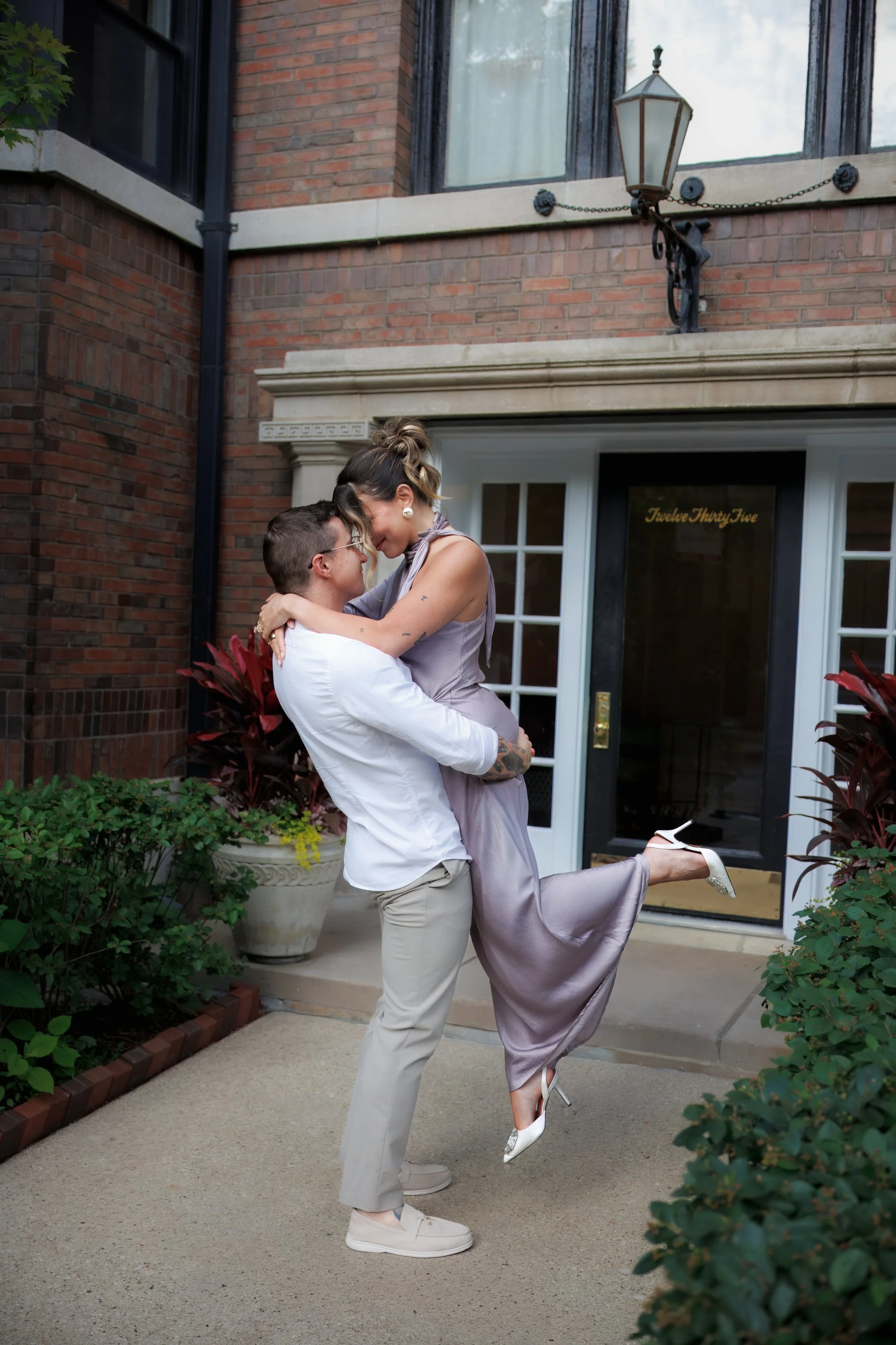 Couple embracing outside a historic Chicago brownstone, with the groom lifting his partner as they smile together during their engagement session.