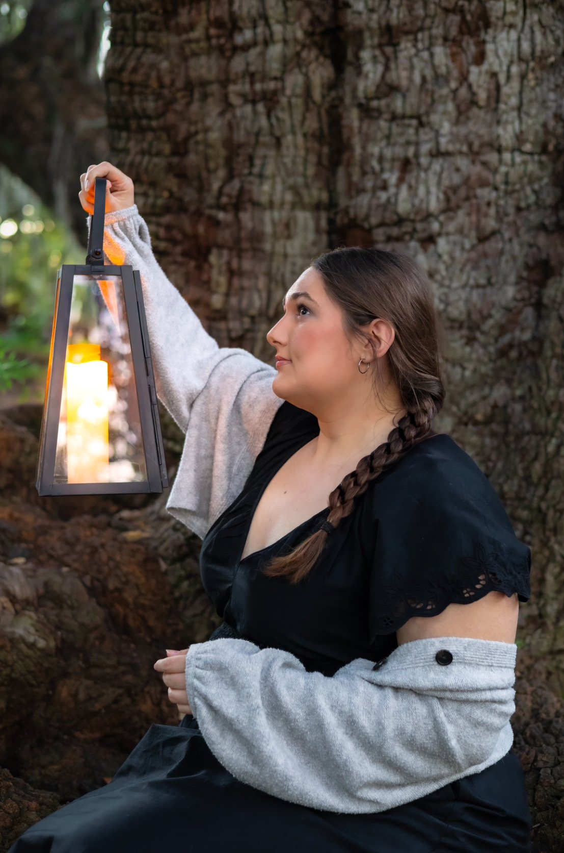 Woman holding a lantern near a tree outdoors.