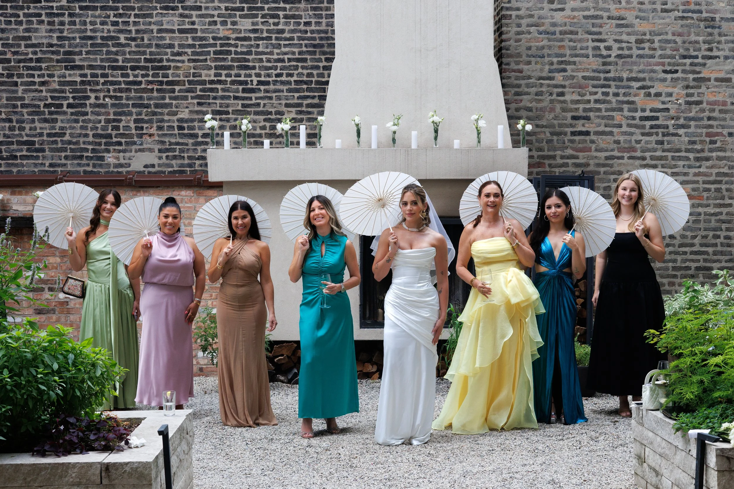 Bridal party standing together during summer wedding with parasols and colorful dresses in outdoor courtyard