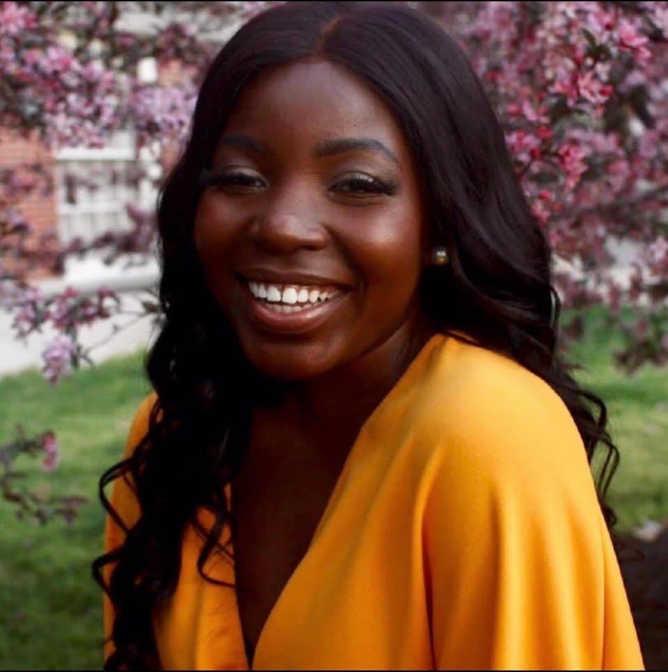 Smiling woman in yellow top with purple flowers in the background.