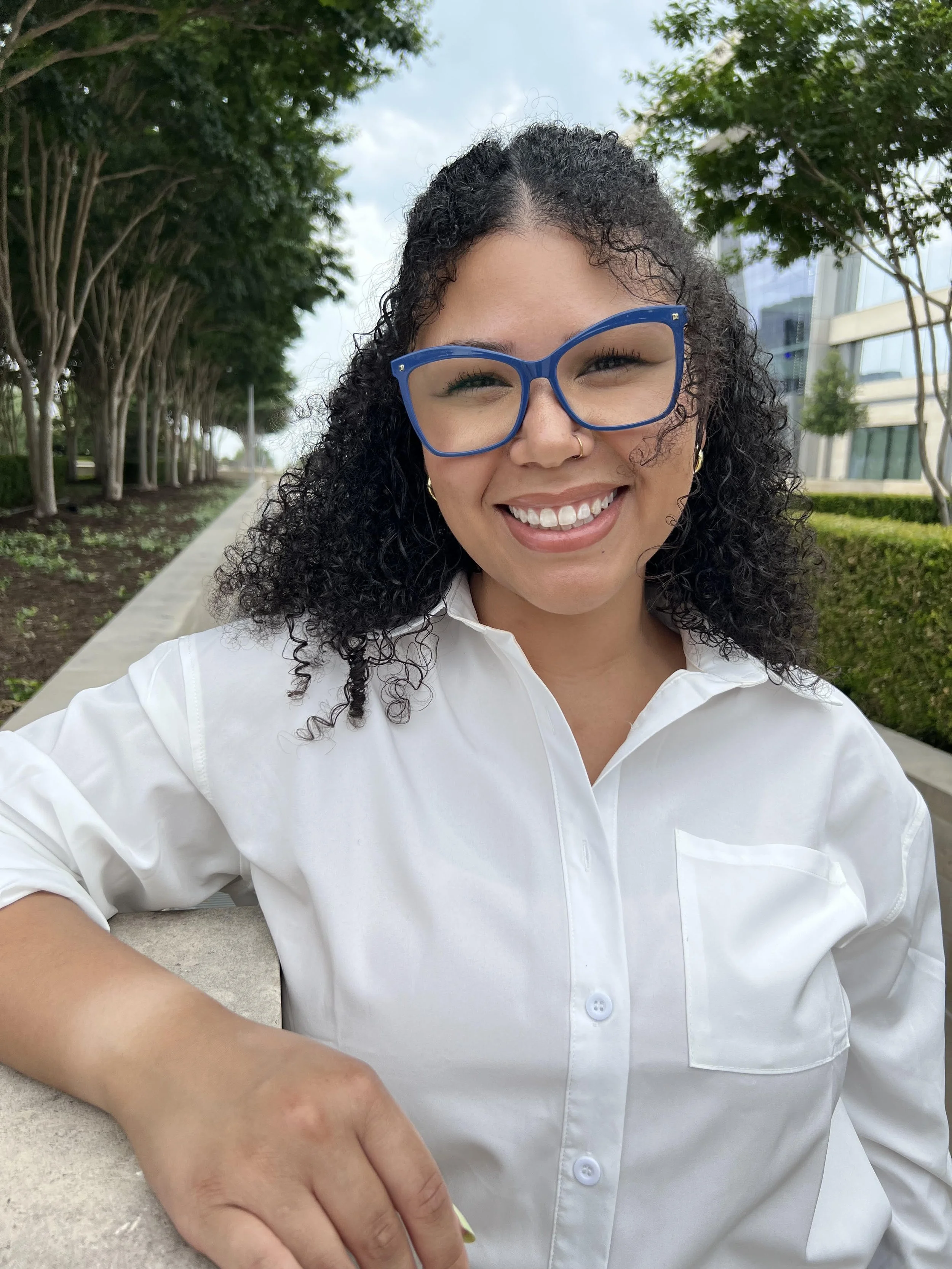 Smiling therapist wearing blue glasses outdoors, representing compassionate, culturally responsive mental health care and holistic counseling services at Relevé Wellness and Counseling.