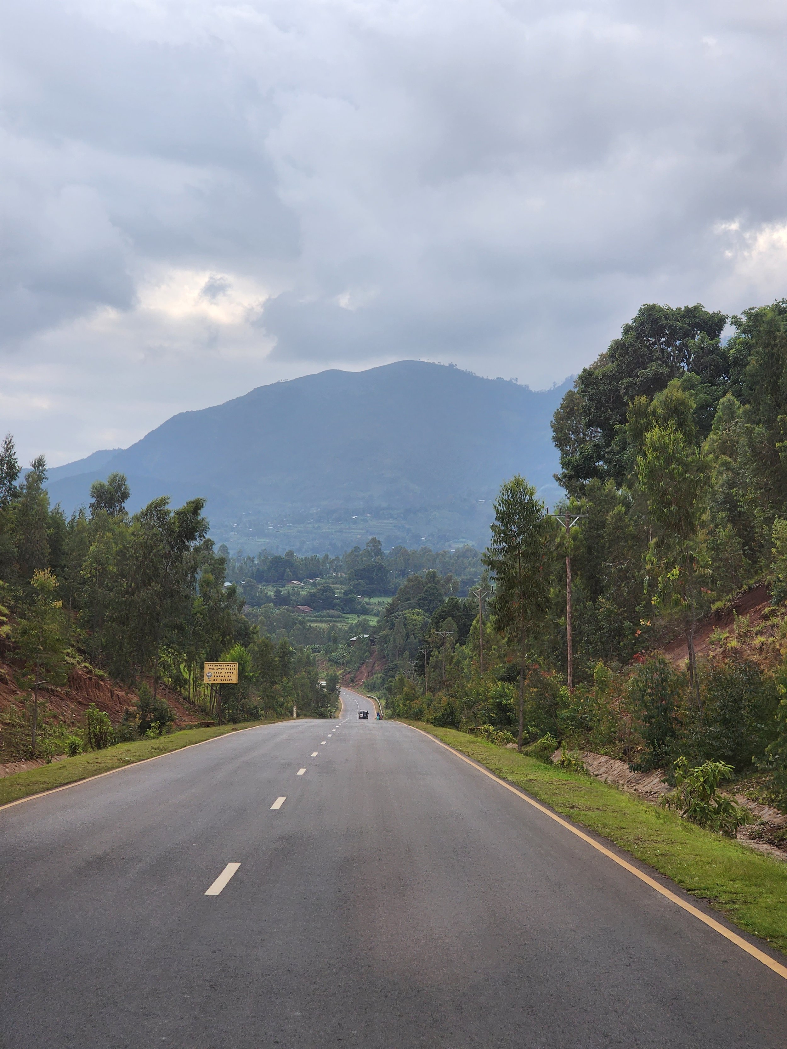 Open road leading through a lush green landscape in Ethiopia with mountains in the background under a cloudy sky.