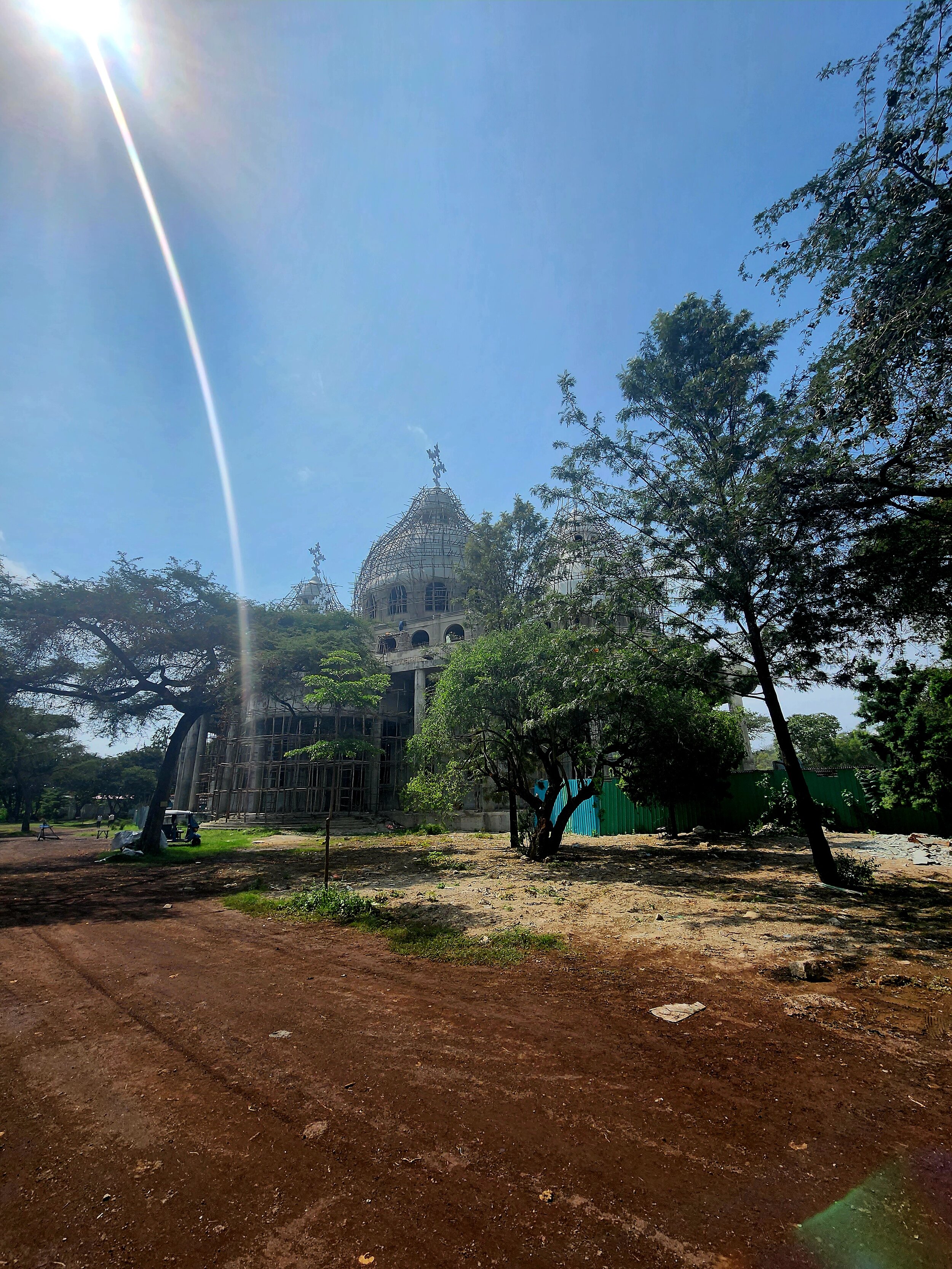 Under-construction Ethiopian Orthodox church with domes and crosses in a sunny, tree-lined area