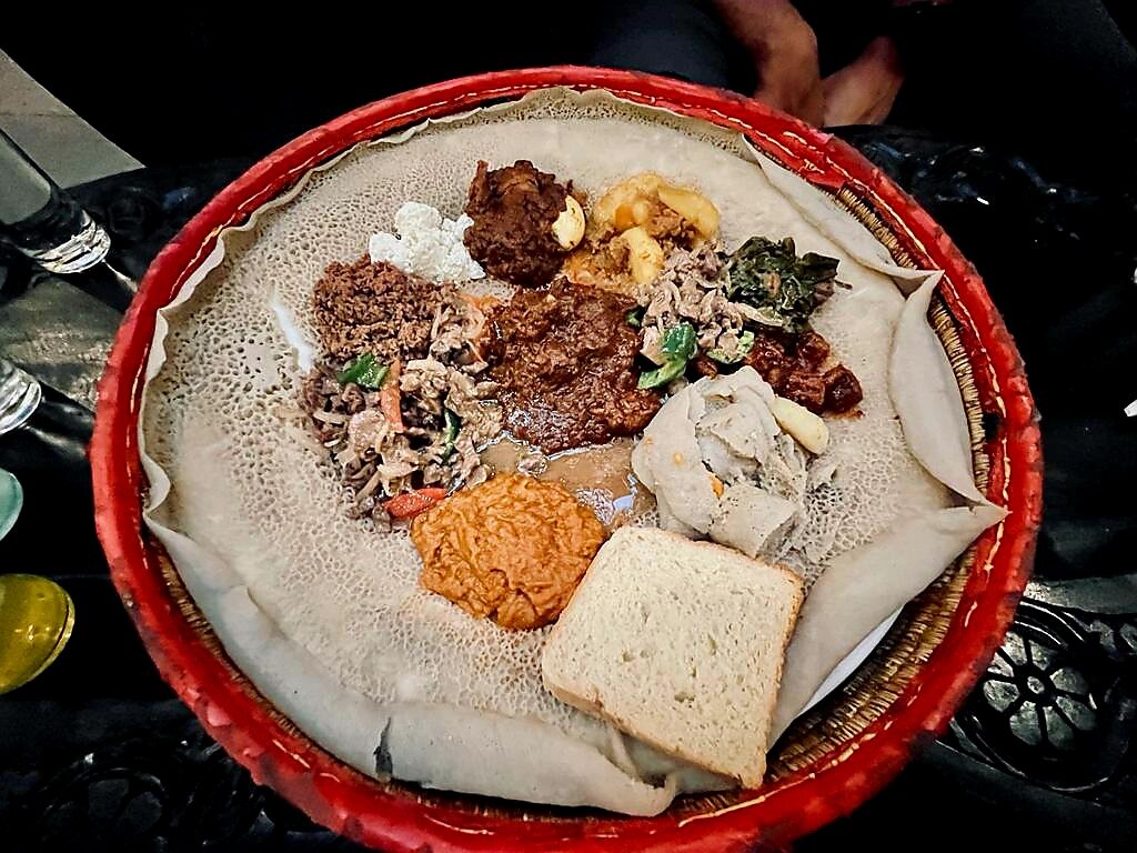Traditional Ethiopian platter featuring injera with a variety of stews and side dishes, served on a woven basket tray.