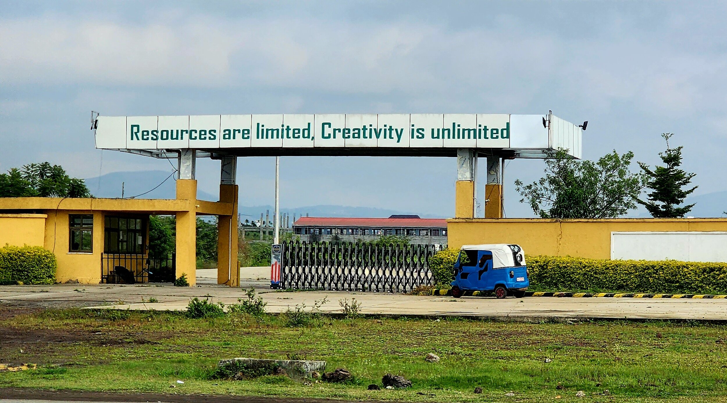Entrance gate with sign "Resources are limited, Creativity is unlimited" and a blue vehicle parked nearby