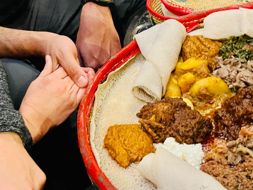 Traditional Ethiopian meal with injera and various dishes on a woven platter, and two people holding hands.