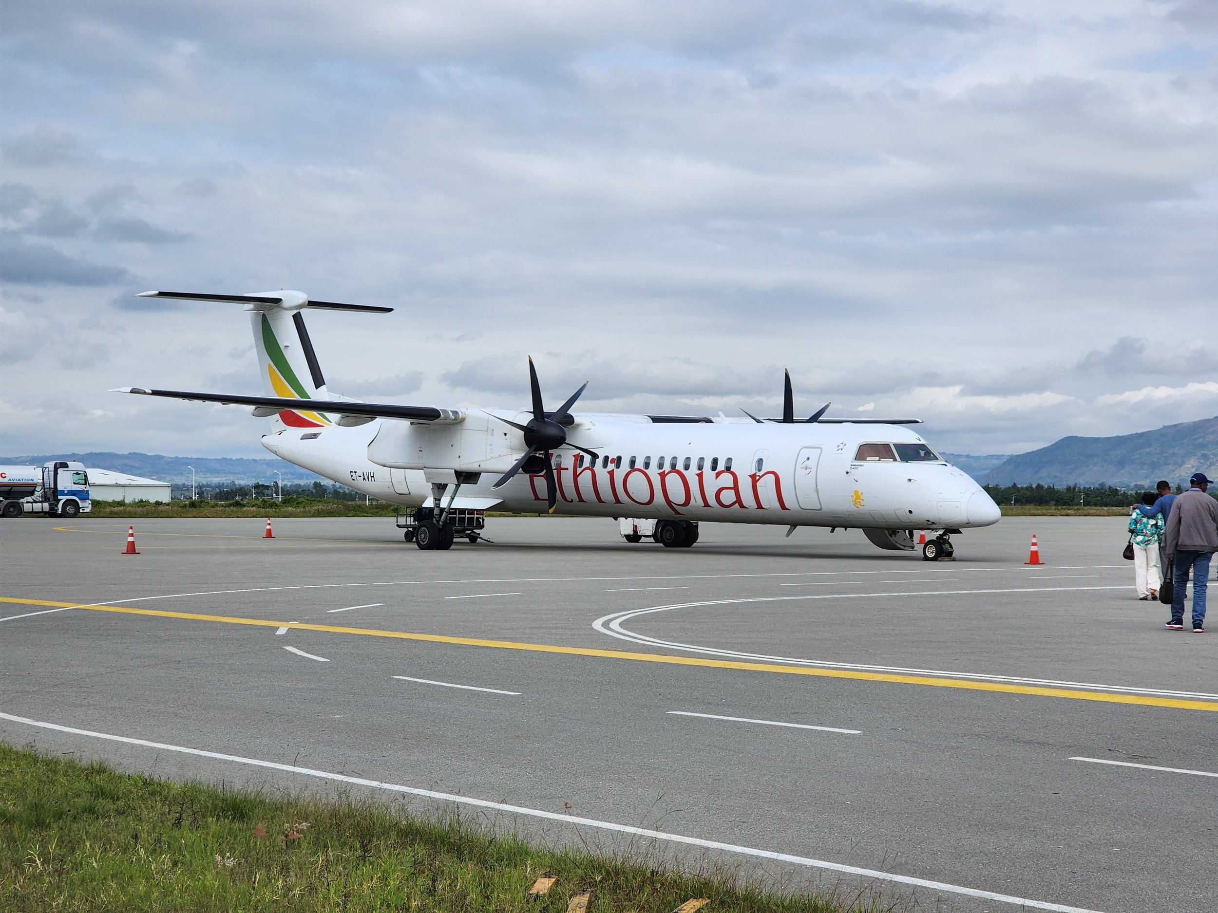 Ethiopian Airlines turboprop aircraft parked on a tarmac with people nearby and a fuel truck in the background.