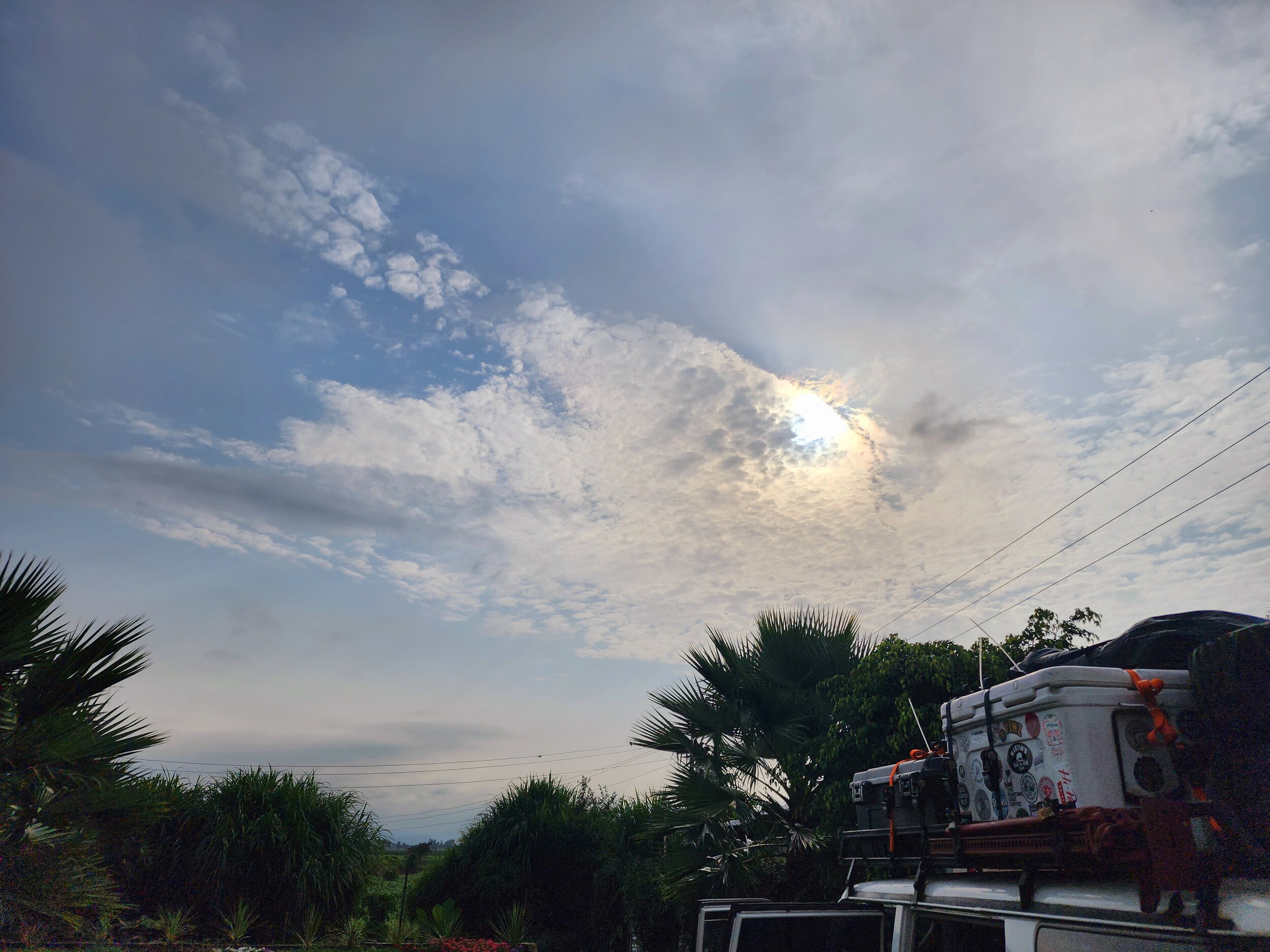 Cloudy sky with sunlight, tropical plants, packed vehicle roof.