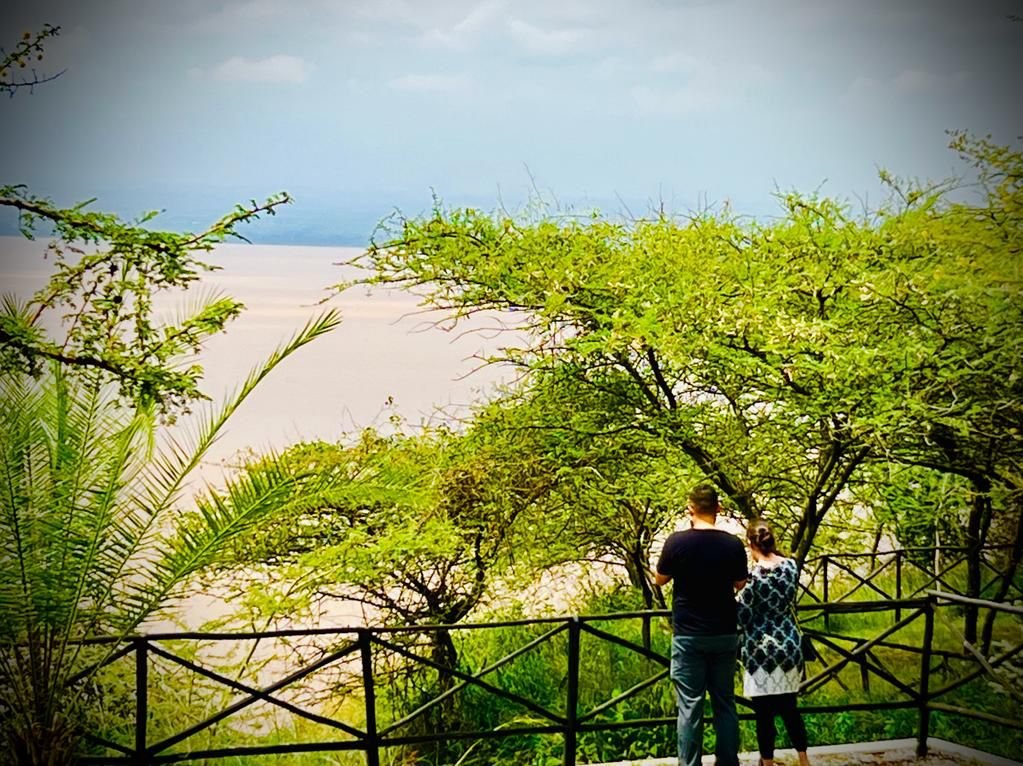Two people standing by a wooden fence overlooking a scenic view of a lake or body of water, surrounded by lush green trees and foliage in a natural setting in Ethiopia.