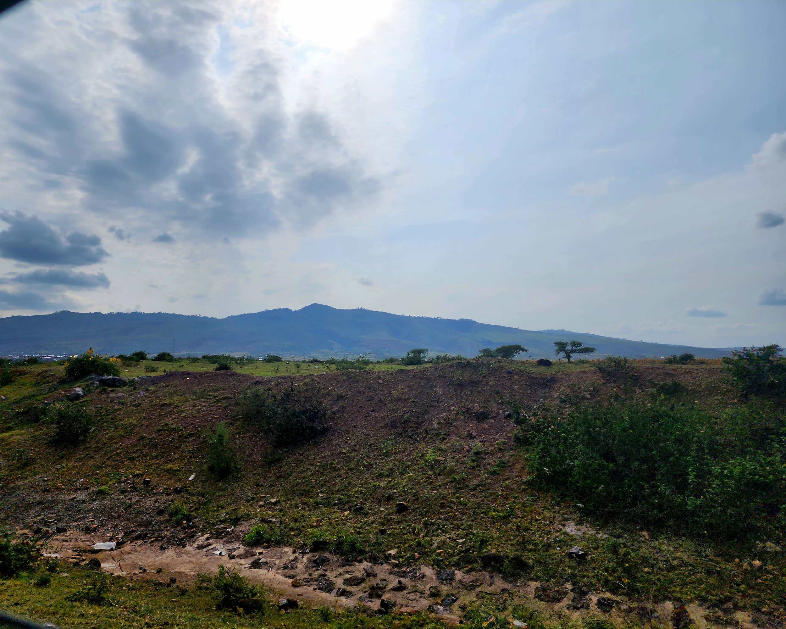 Hilly Ethiopian landscape with sparse vegetation and mountains from the Great Rift Valley under a cloudy sky.