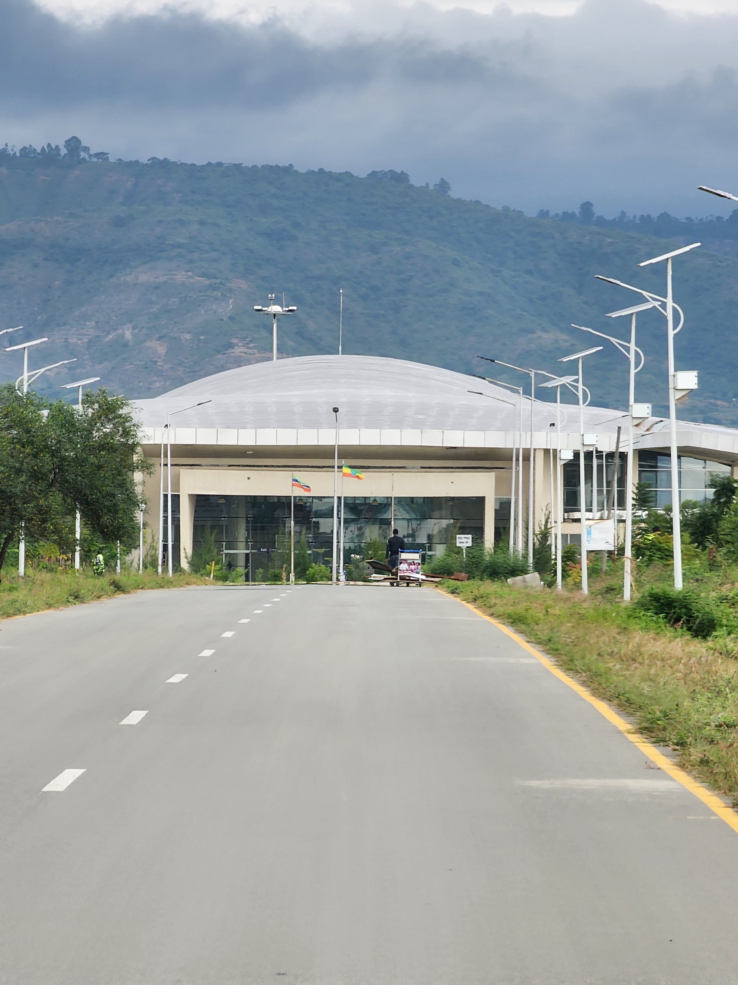 Road leading to a modern building with a dome roof, surrounded by green hills and streetlights. Flags are visible near the entrance in Ethiopia.