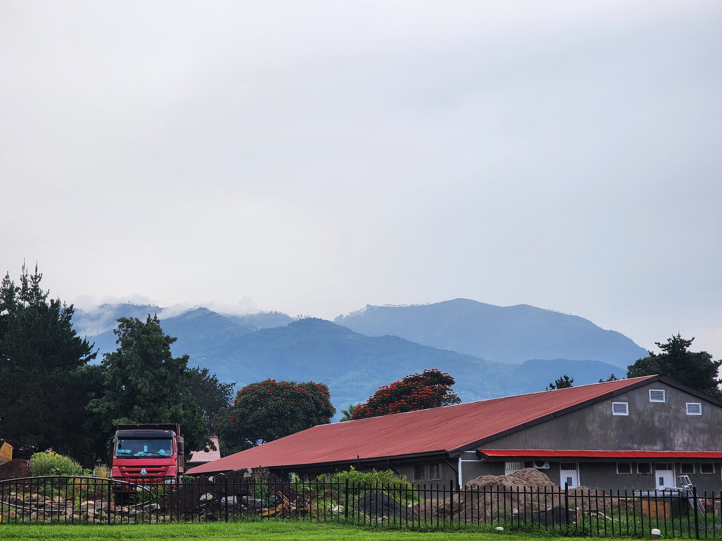 Landscape with a red-roofed building and truck in foreground, mountains and trees in background at Soddo Christian Hospital in Ethiopia.