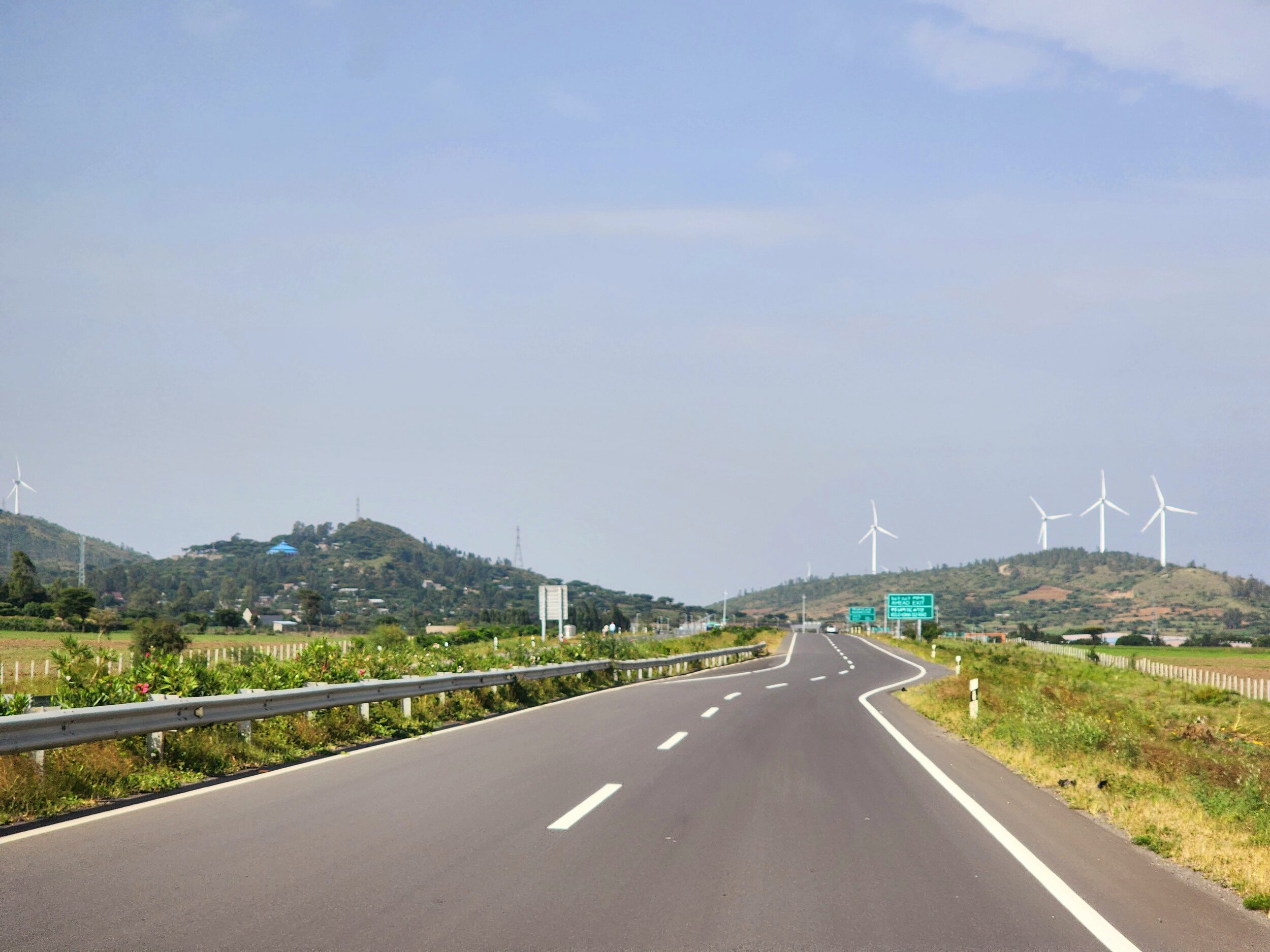 Open road with wind turbines on hills in the background, surrounded by greenery and clear sky in Ethiopia.