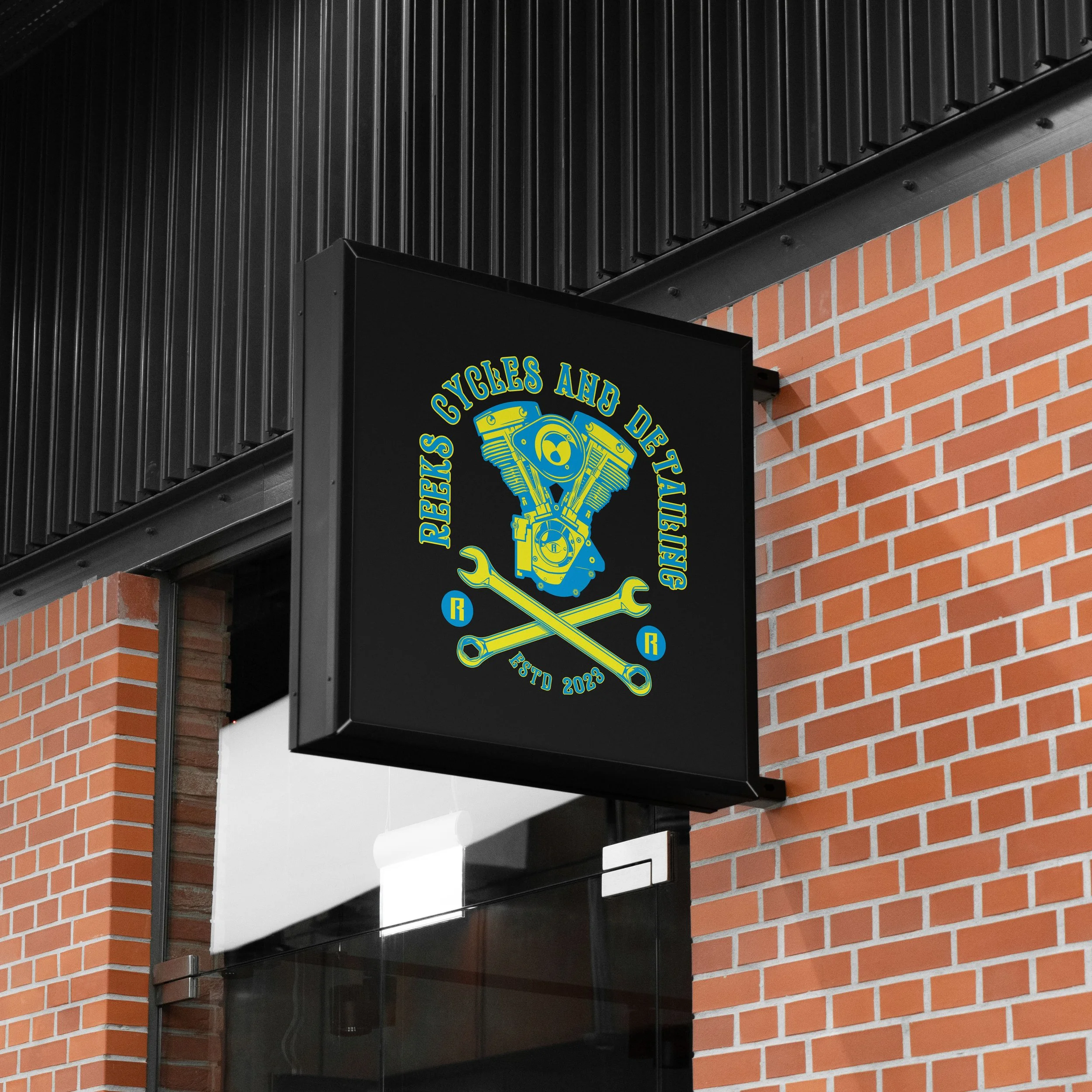 Storefront sign for 'Reks Cycles and Detailing' featuring a motorcycle engine and crossed wrenches.