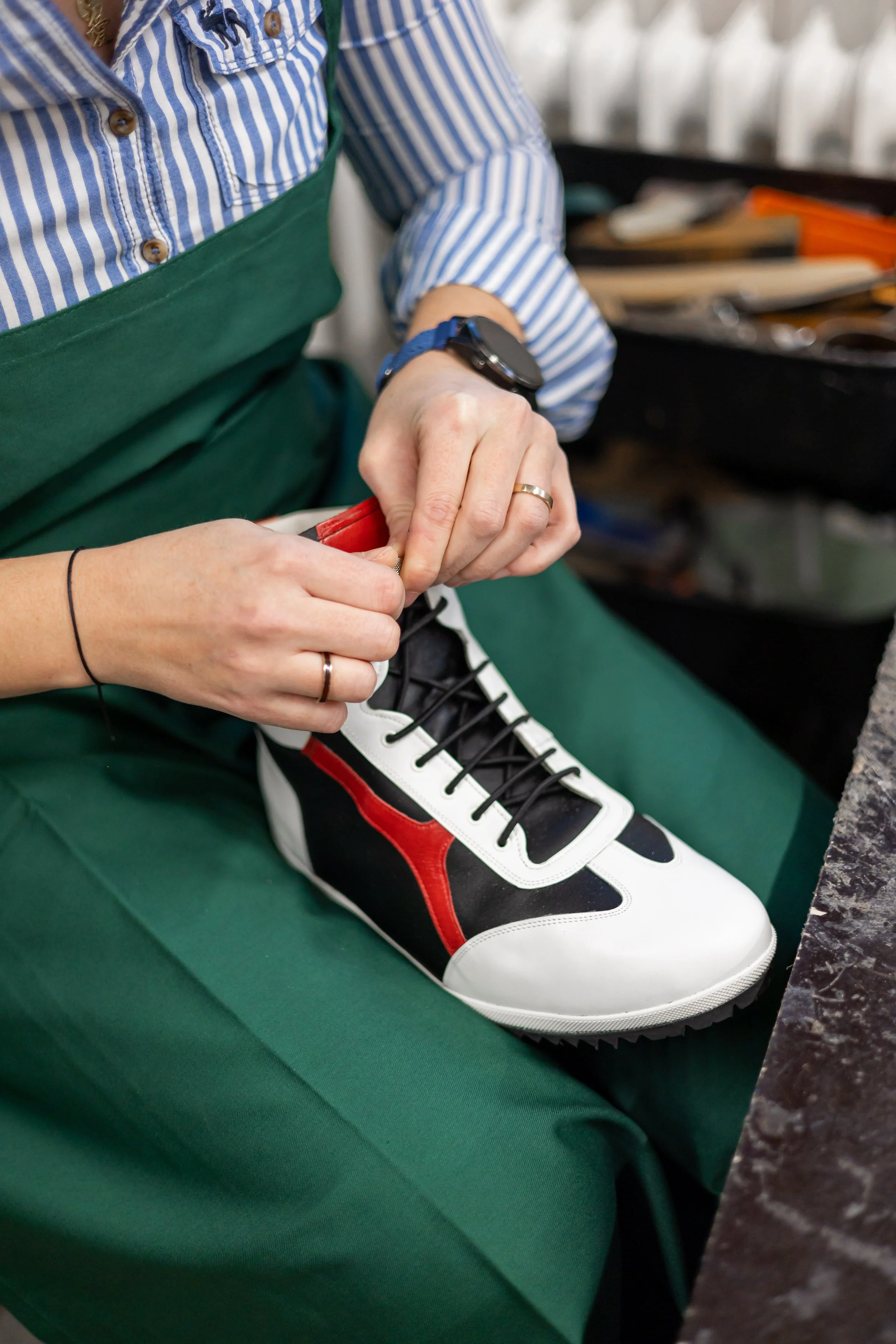 Geschäftsführerin Eva Brüll Plönnes bindet Schnürsenkel an einem orthopädischen Schuh, sie trägt eine grüne Schürze und eine blaue Uhr.