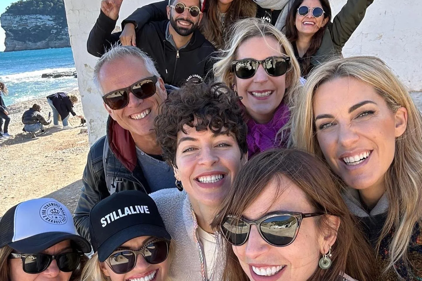 Grupo de personas disfrutando en la playa, tomando una selfie frente a la mar, todos con gafas de sol y sonriendo.