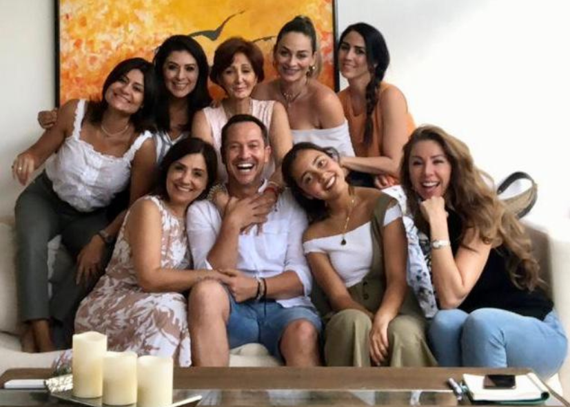 Grupo de personas sonrientes y felices en una reunión social en un salón con decoración amarilla y un cuadro en la pared.