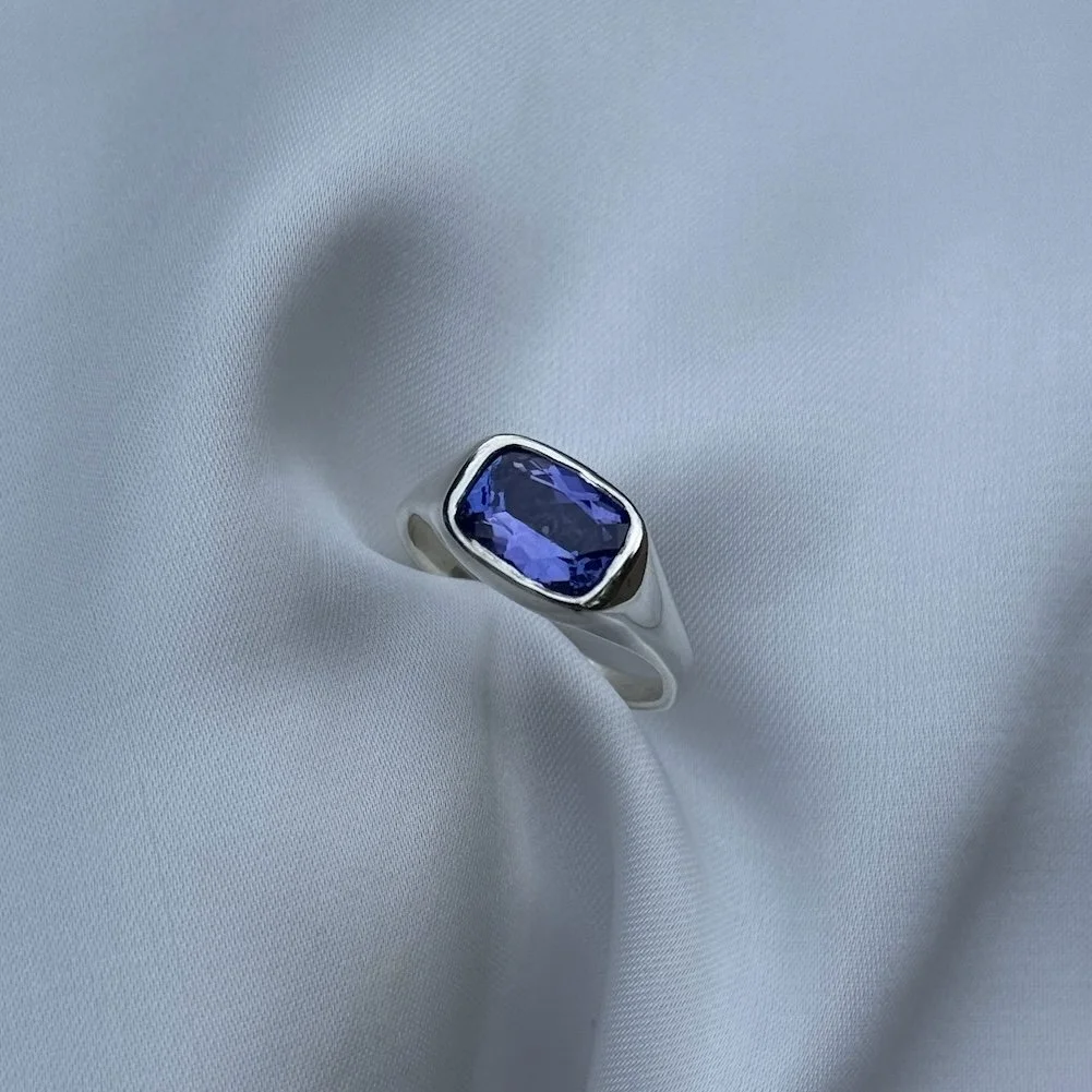 Silver ring with a large rectangular tanzanite on a white satin background.