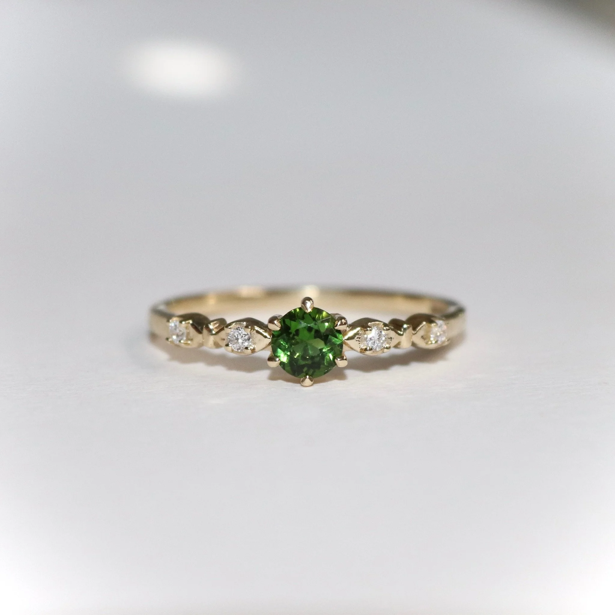 A bespoke engagement ring with a green tsavorite and small side lab grown diamonds in a claw set ring.