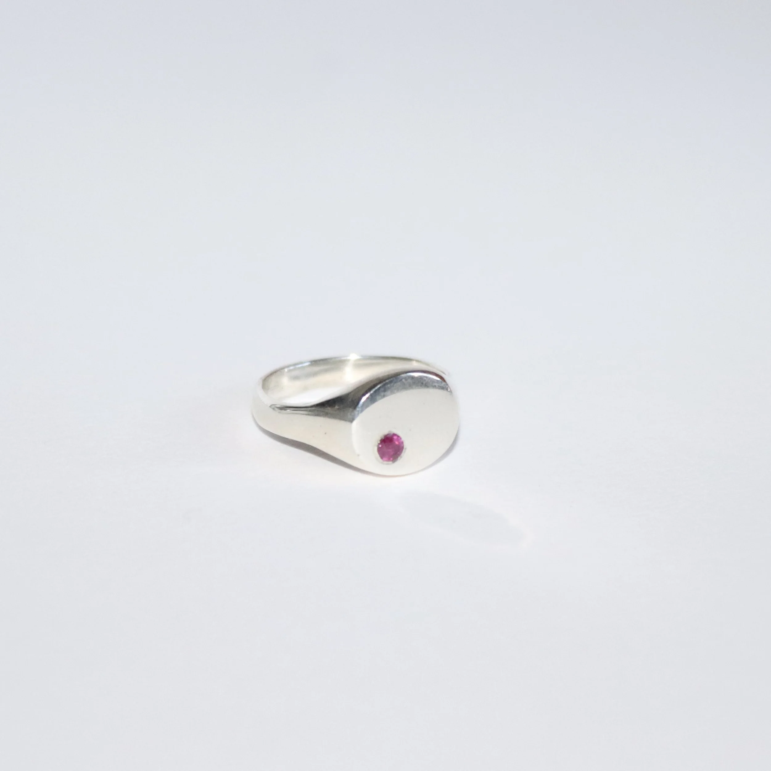 Silver acrostic ring with a round face and a ruby (inital r) gemstone in the center.