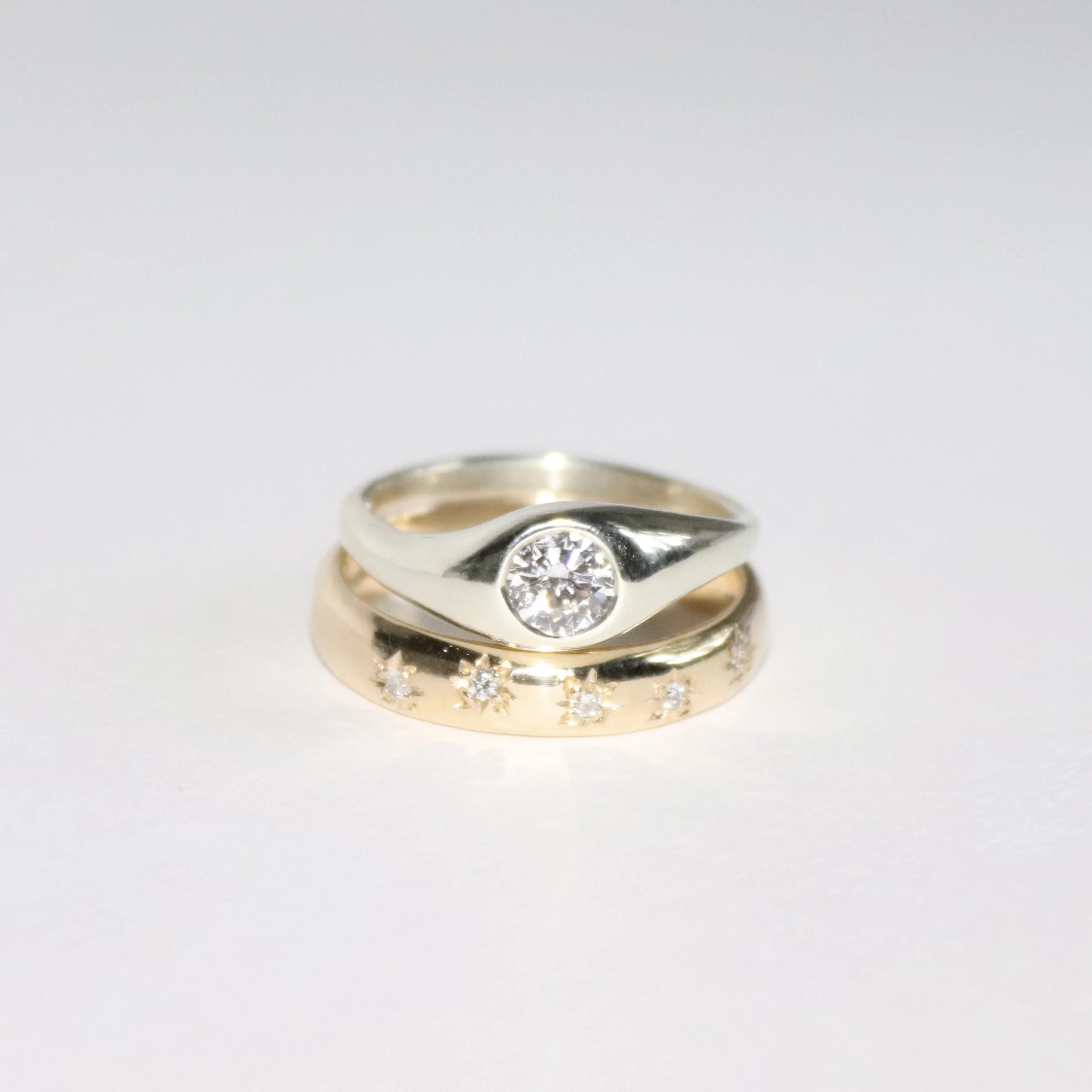 Stacked gold and silver wedding and engagement rings with diamonds on a white background.