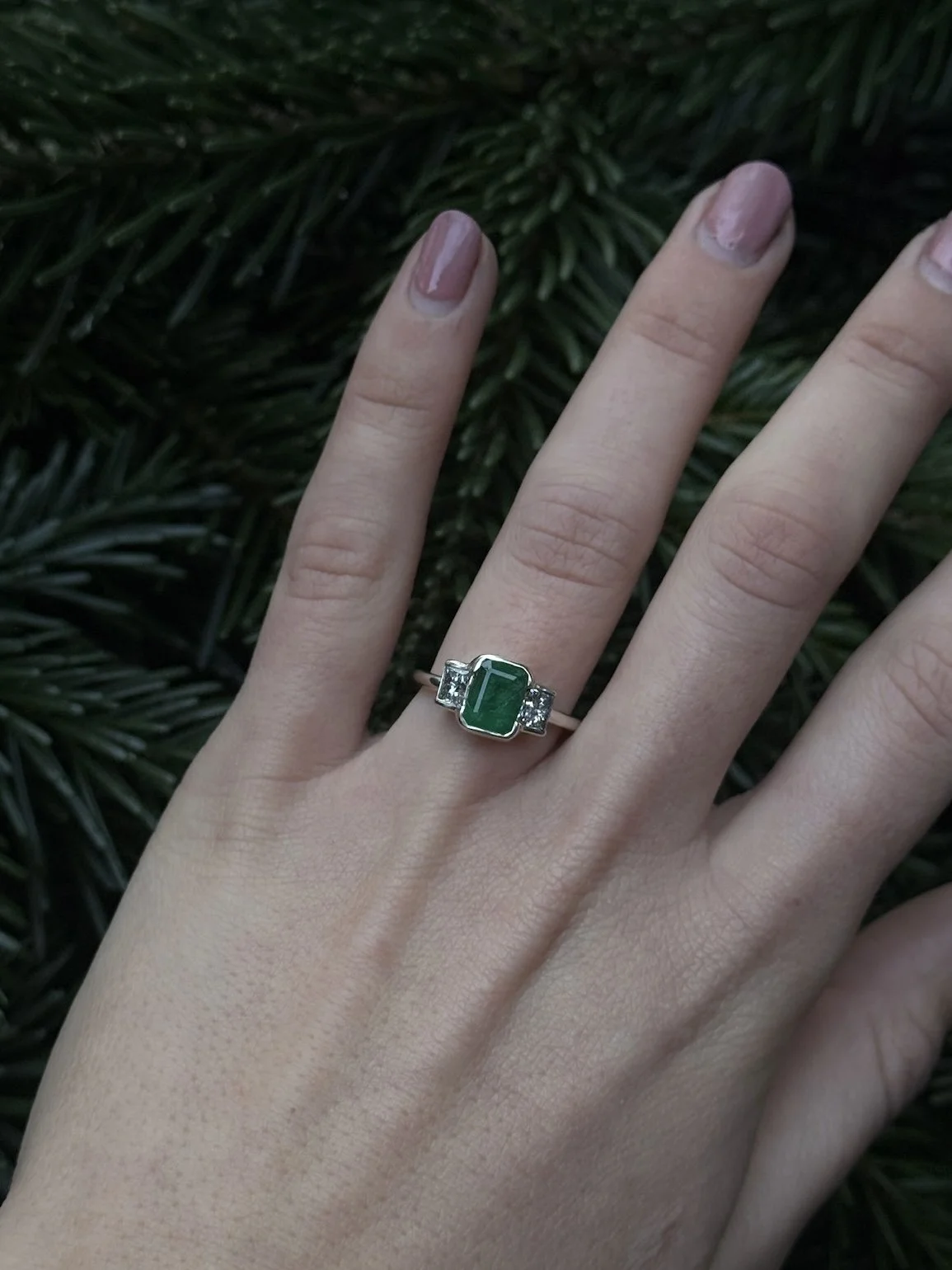 Close-up of a hand wearing a 9ct white gold emerald cut green engagement ring and two diamonds set on either side.