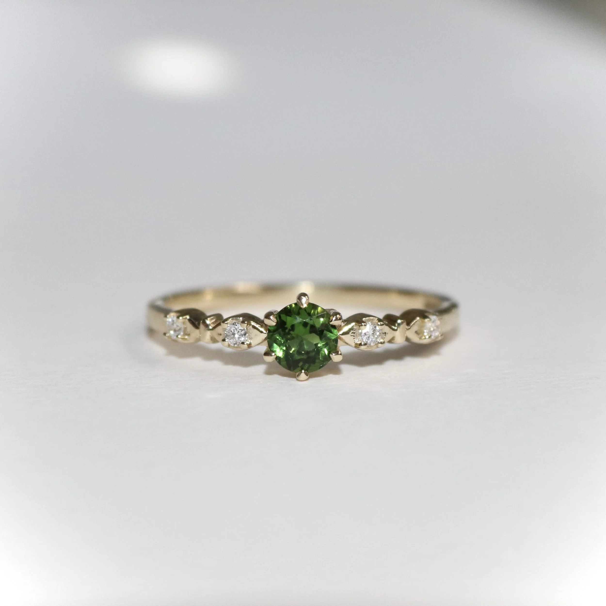 Close-up of a 9ct gold engagement ring with a large green tsavorite gemstone and smaller lab grown diamonds set in the sides of the band.