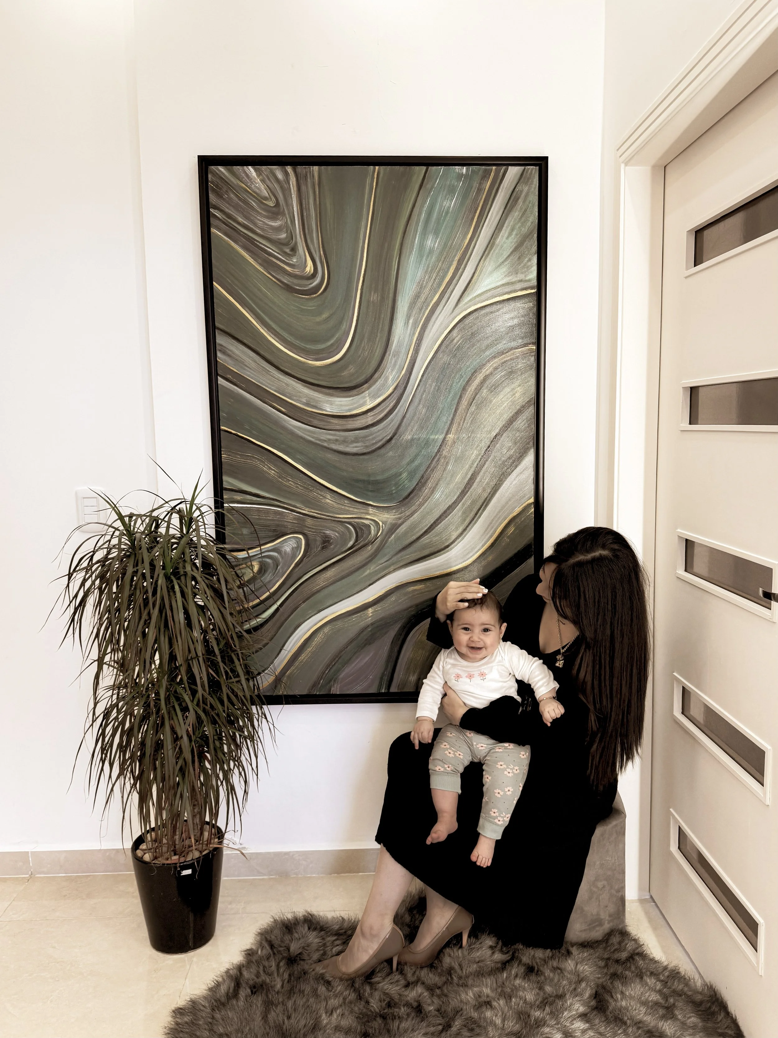 Artist Mayssam holding her daughter Sophia in front of a large textured abstract painting, expressing the connection between motherhood and artistic creation at mKunstraum