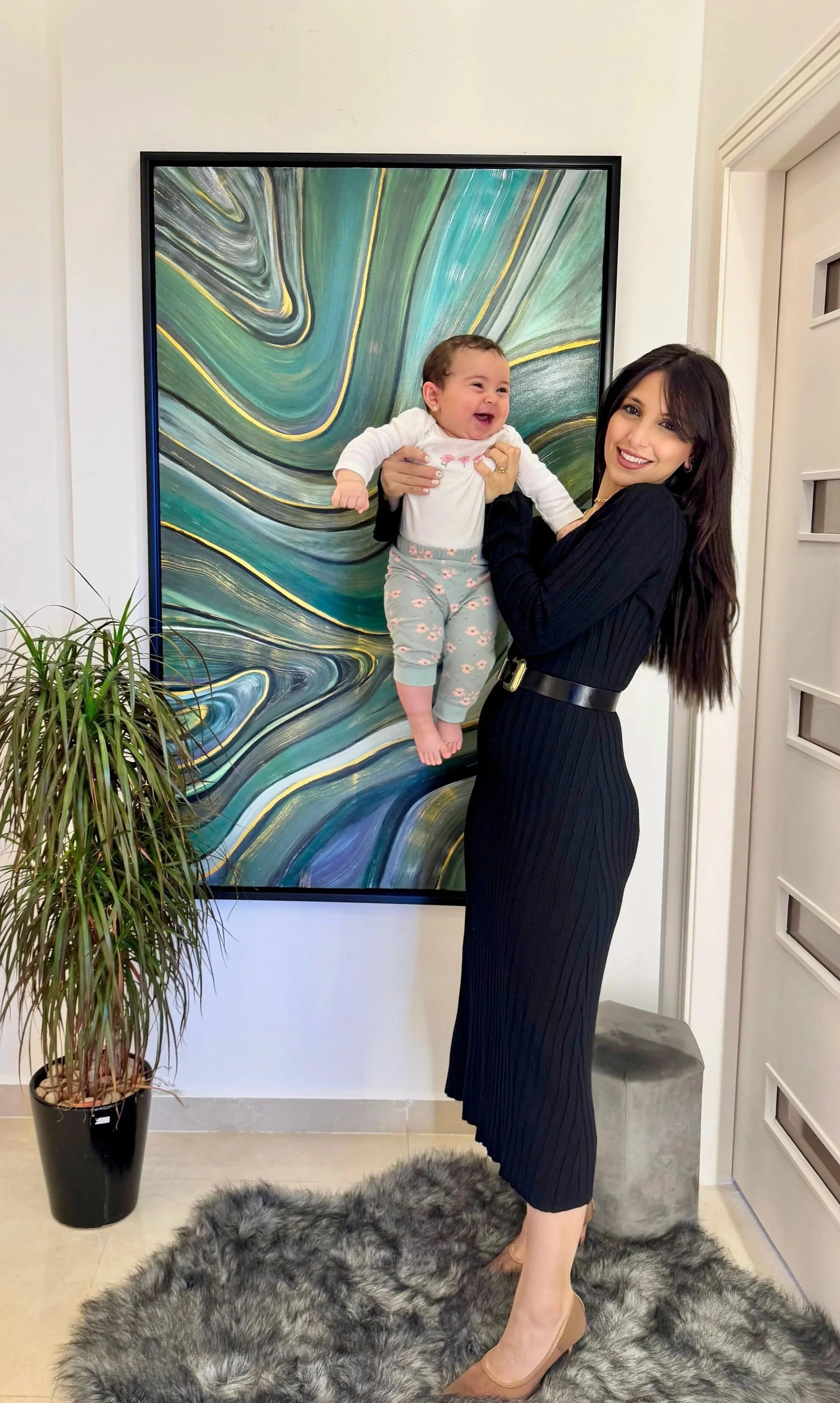 Artist Mayssam holding her daughter Sophia in front of a textured abstract artwork, reflecting motherhood and inspiration behind mKunstraum