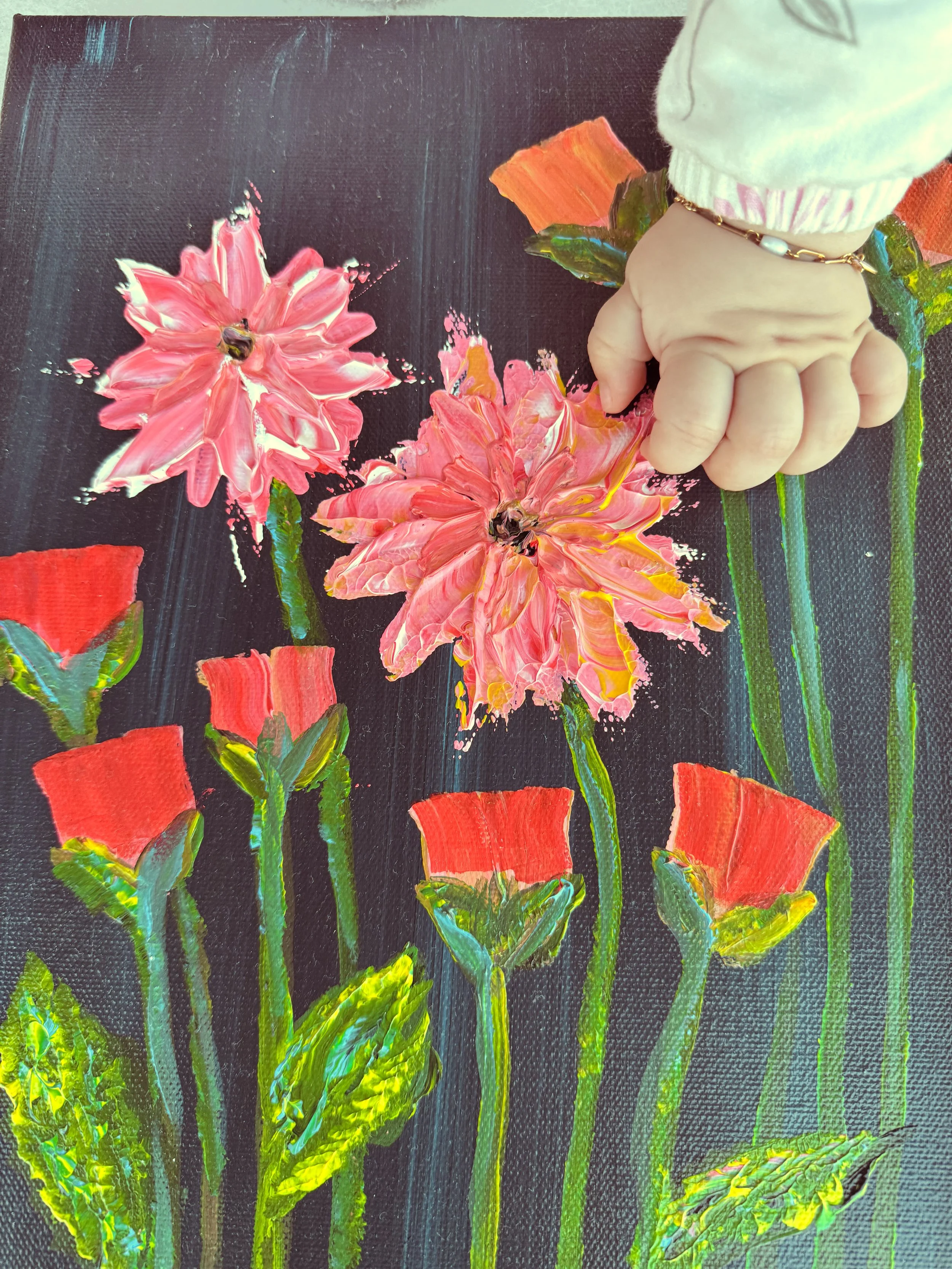 Close-up of artist Mayssam’s textured floral painting with her daughter Sophia’s hands exploring the surface, capturing touch, motherhood, and the emotional connection behind mKunstraum