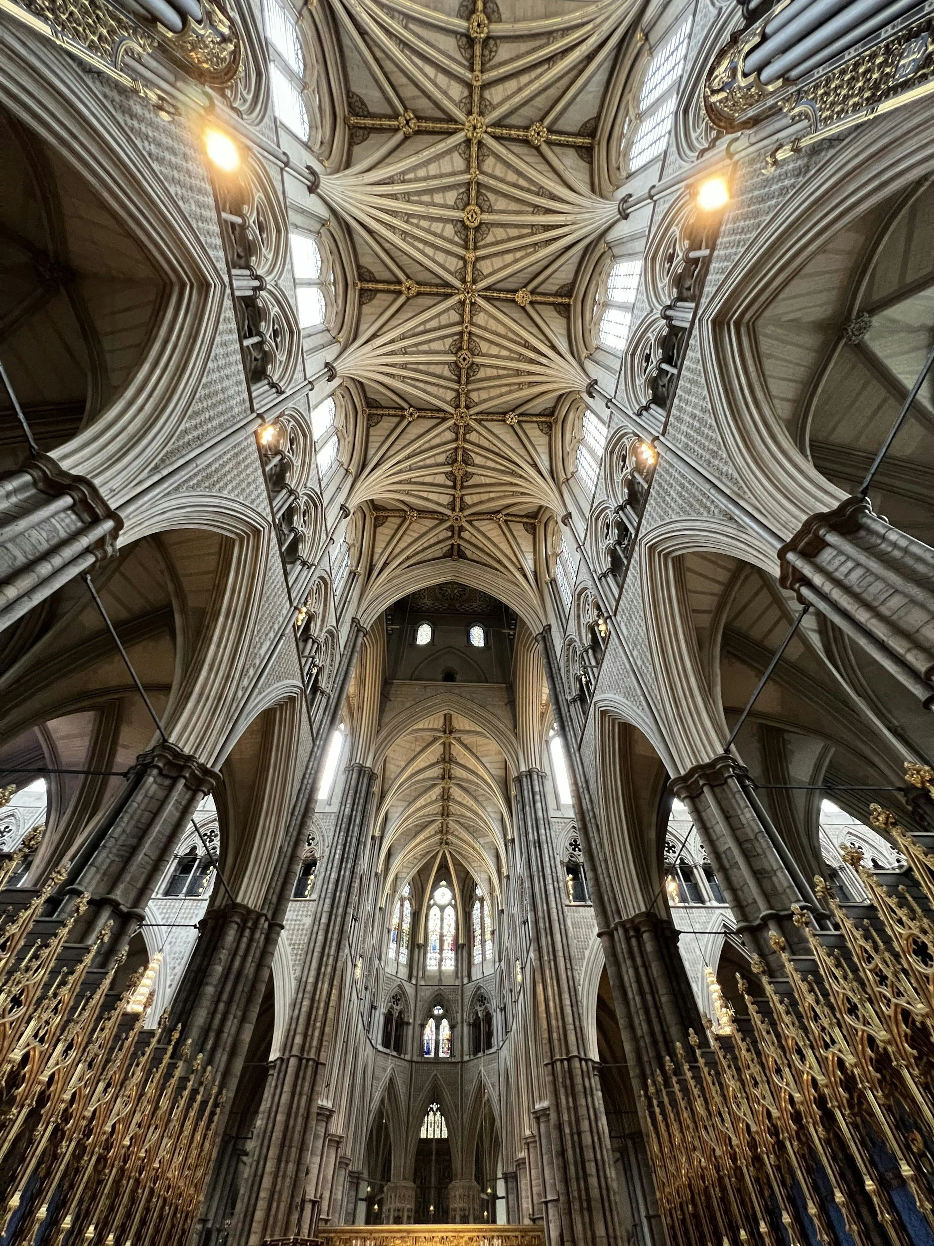 Interior view of a Gothic cathedral ceiling with intricate ribbed vaults, stained glass windows, and ornate gold accents.